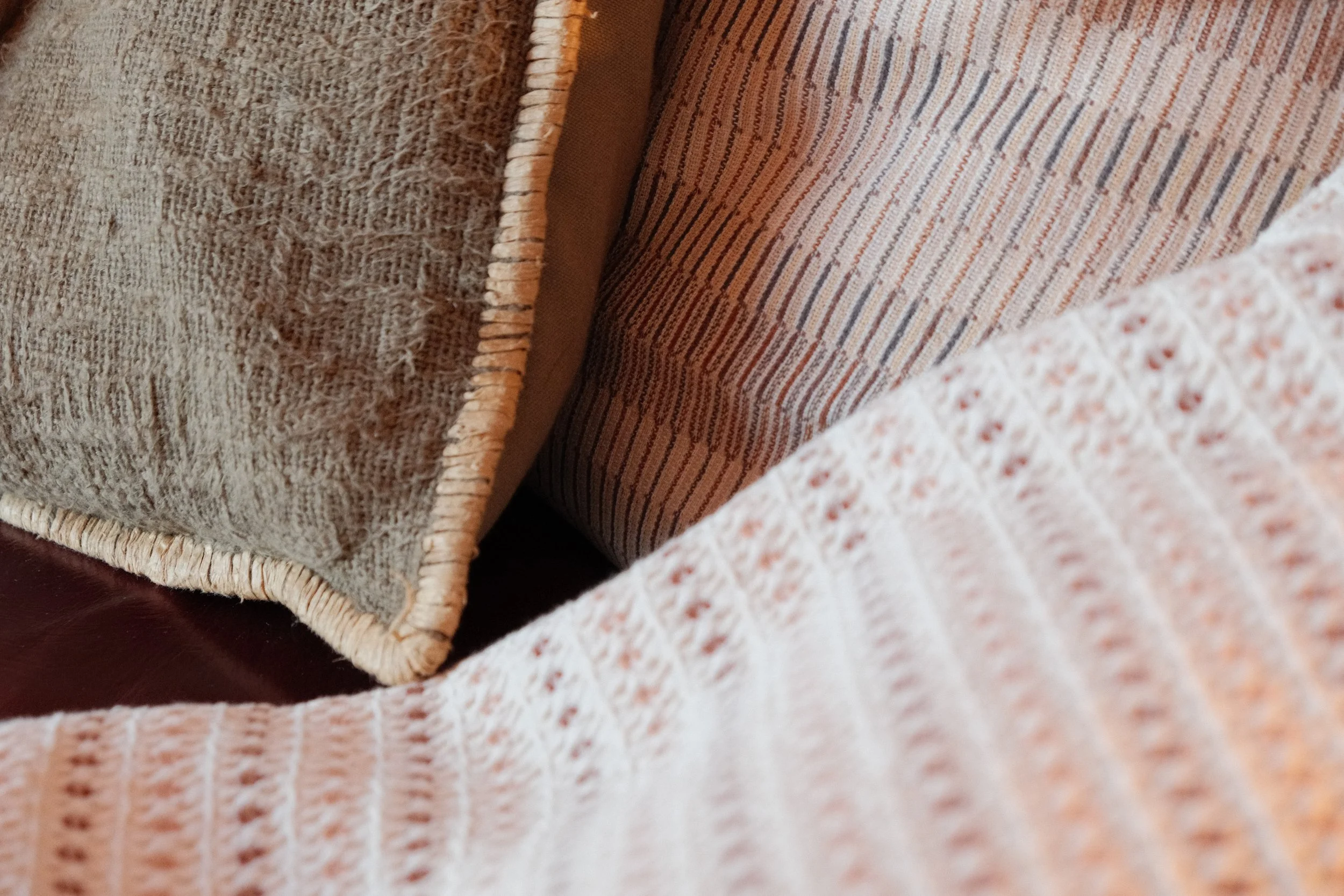 Nahaufnahme von Kissen und Decken auf einem Sofa, mit verschiedenen Texturen und Mustern in warmen Farben.