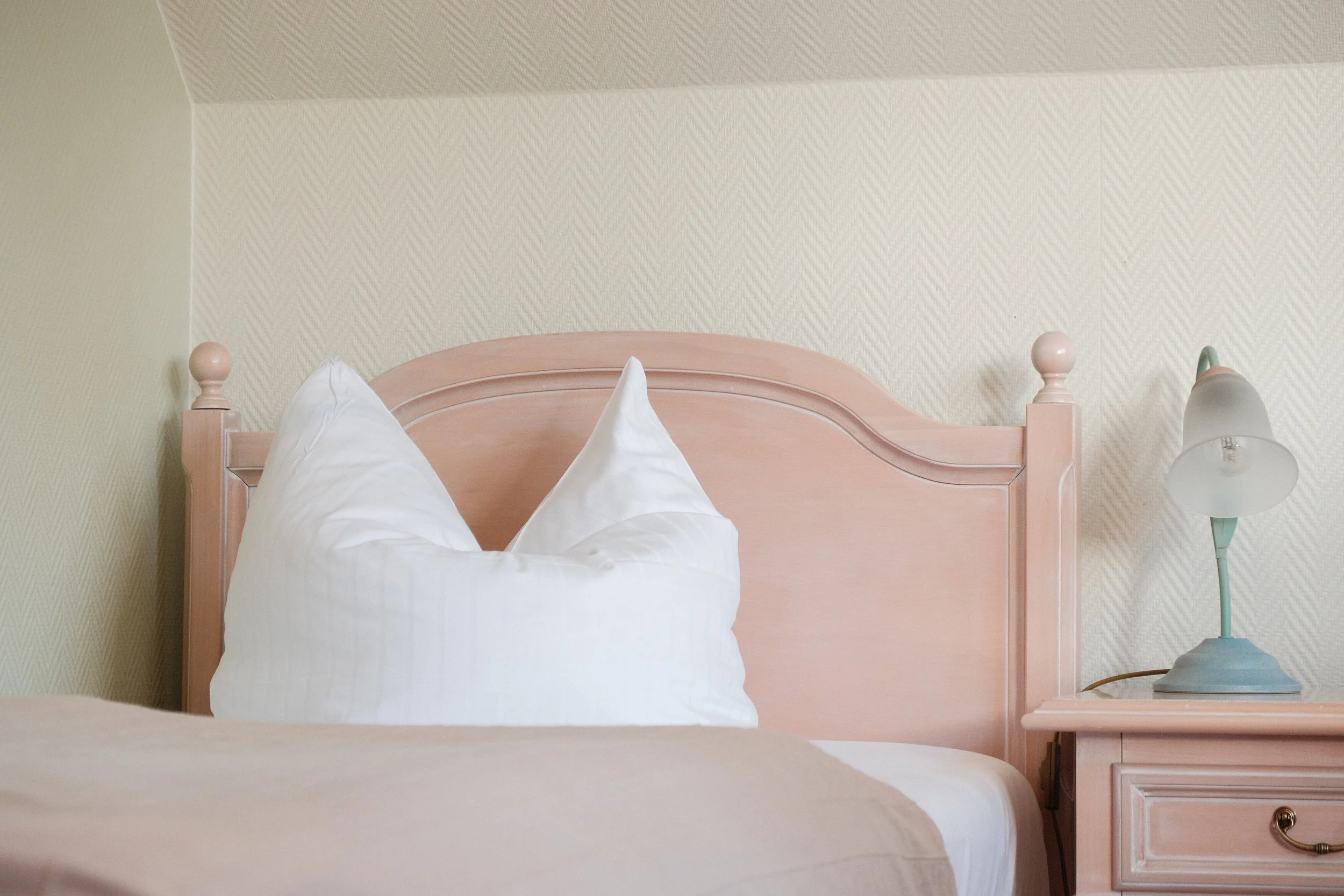 Bett mit weißen Kissen, pinkes Kopfteil, grüner Nachttischlampe, beige Bettwäsche, beige Wand