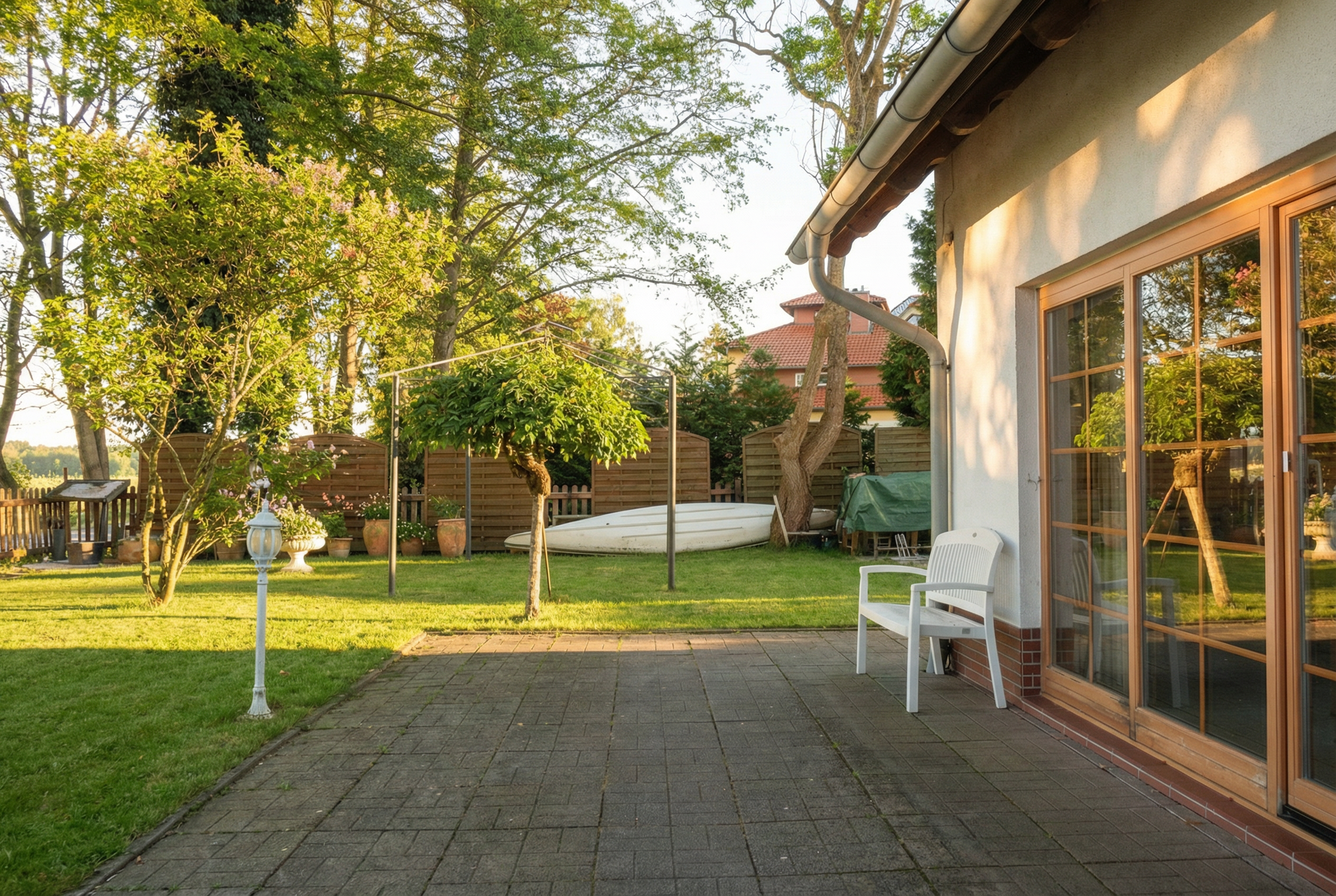 Gartenmit Sitzbank, Bäume, Rasen, Gartenzaun, Boot, Gartenmöbel, Haus mit Terrasse, Sonnenschein.