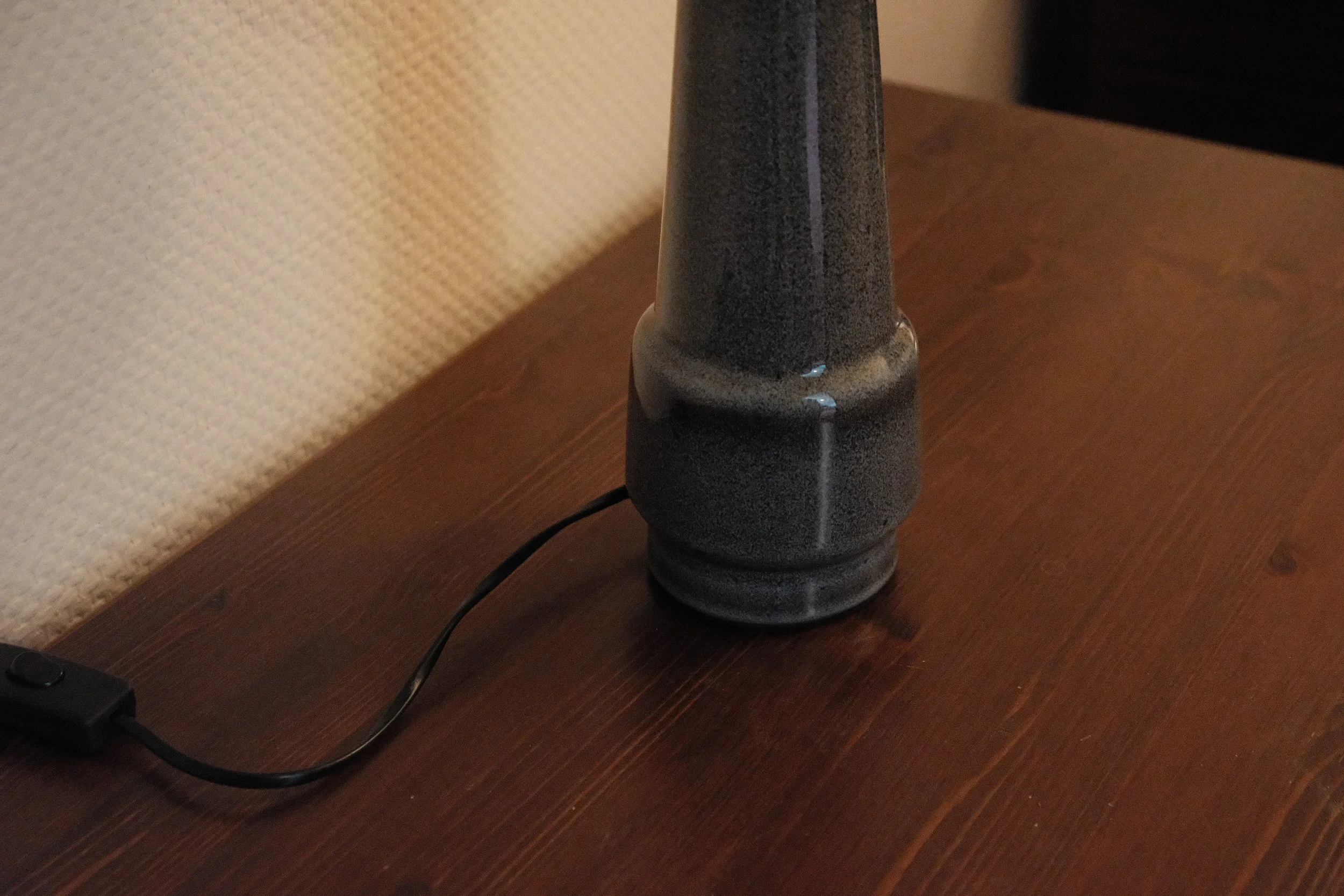 Schwarzer Lampenfuß auf einem Holztisch mit anliegendem Kabel
