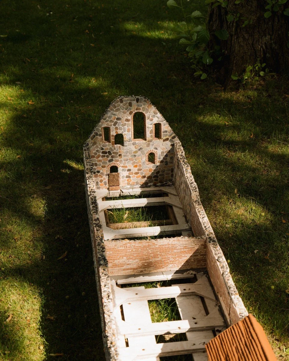 Miniaturmodell einer alten Steinkirche auf grünem Rasen, mit Sonnenlicht und Schatten