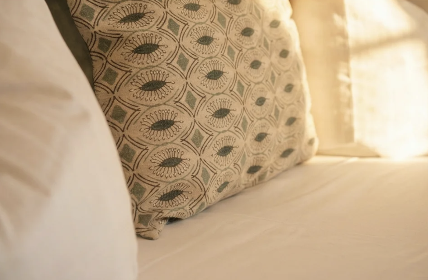 Ein Bett mit einer beige Bettdecke und einem dekorativen Kissen mit einem Muster aus schwarzen und blauen Muscheln auf einem weißen Hintergrund.