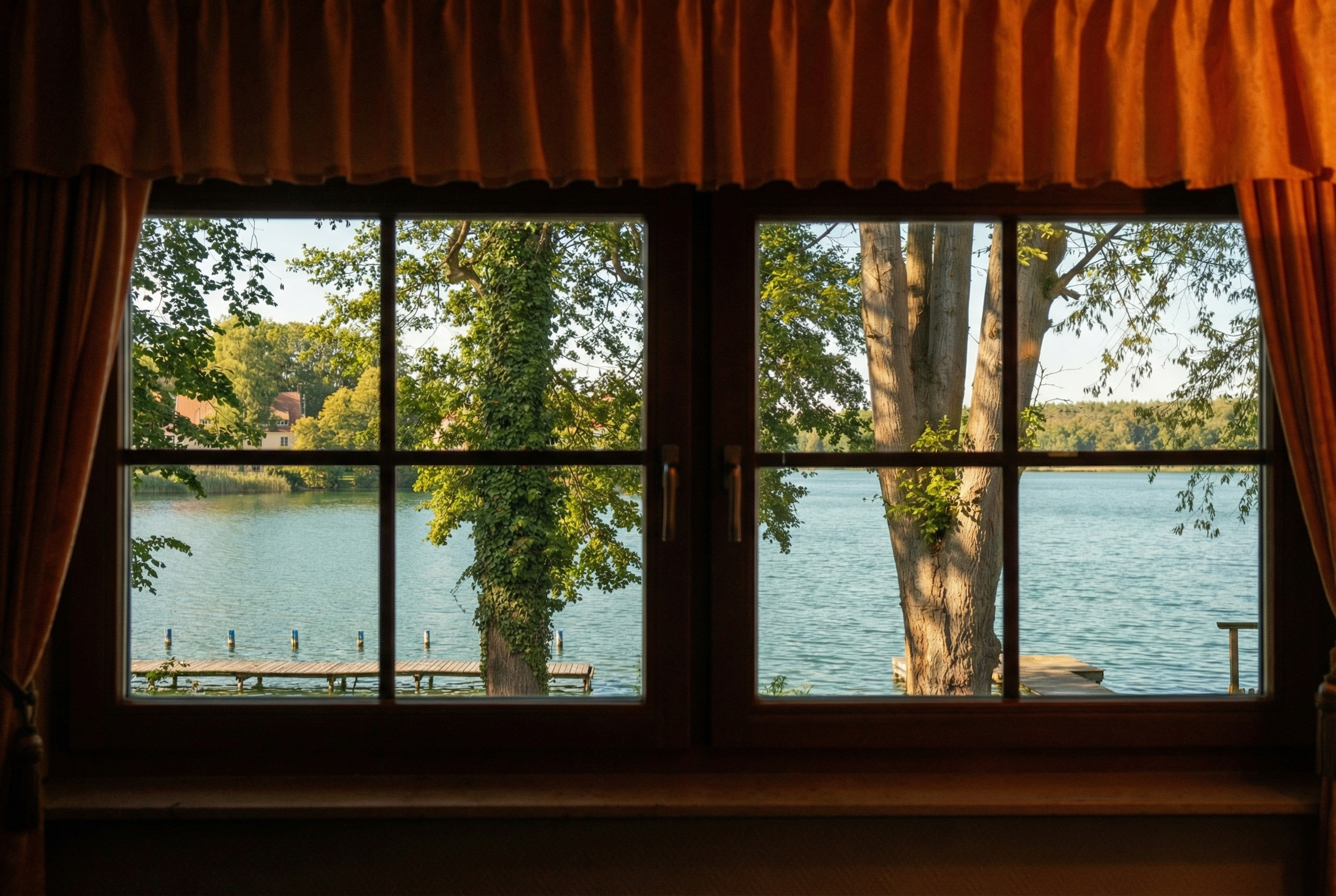 Blick durch ein Fenster auf einen See mit Bäumen und eine kleine Landungsbrücke.