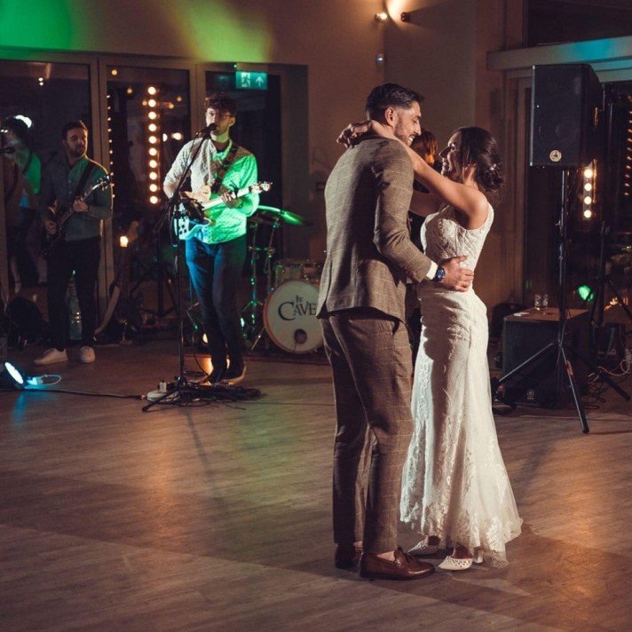 A newlywed couple dancing at their wedding reception with a live band playing in the background.