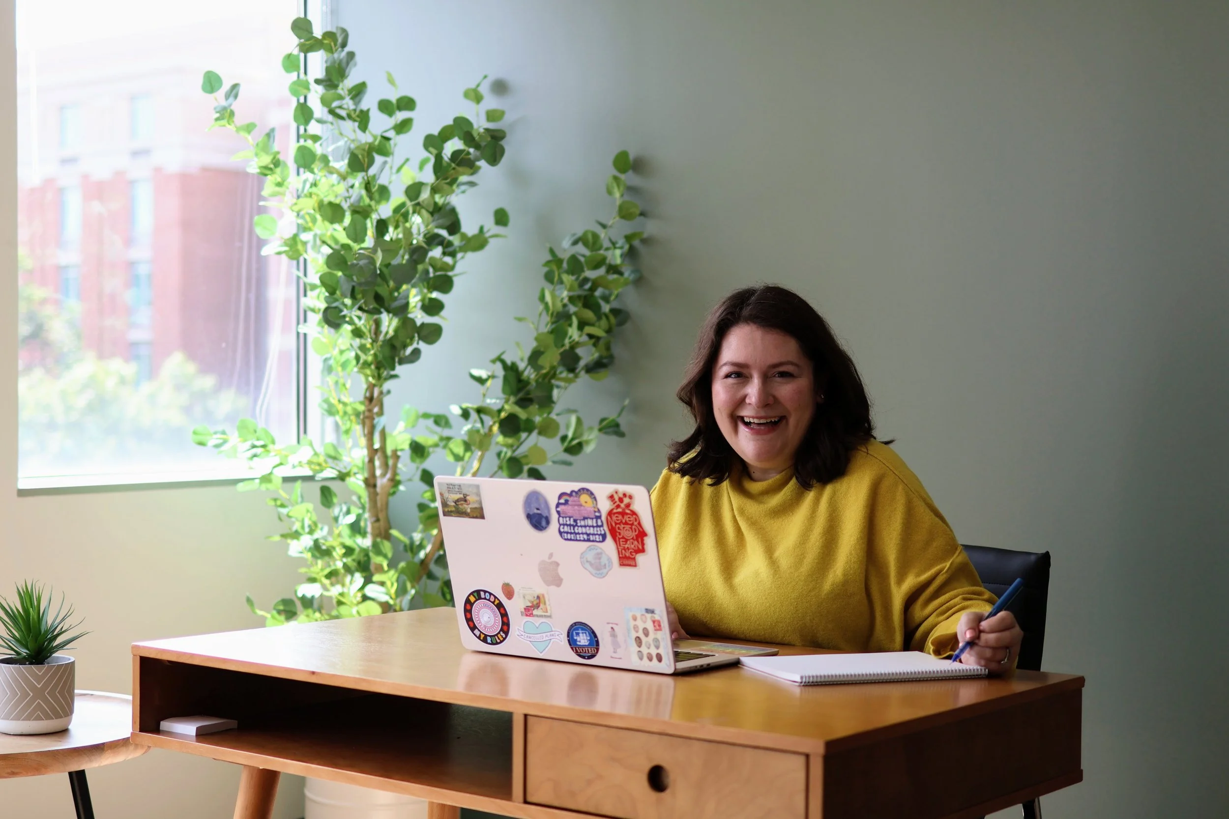 Therapist smiling while sitting at desk with computer and notebook