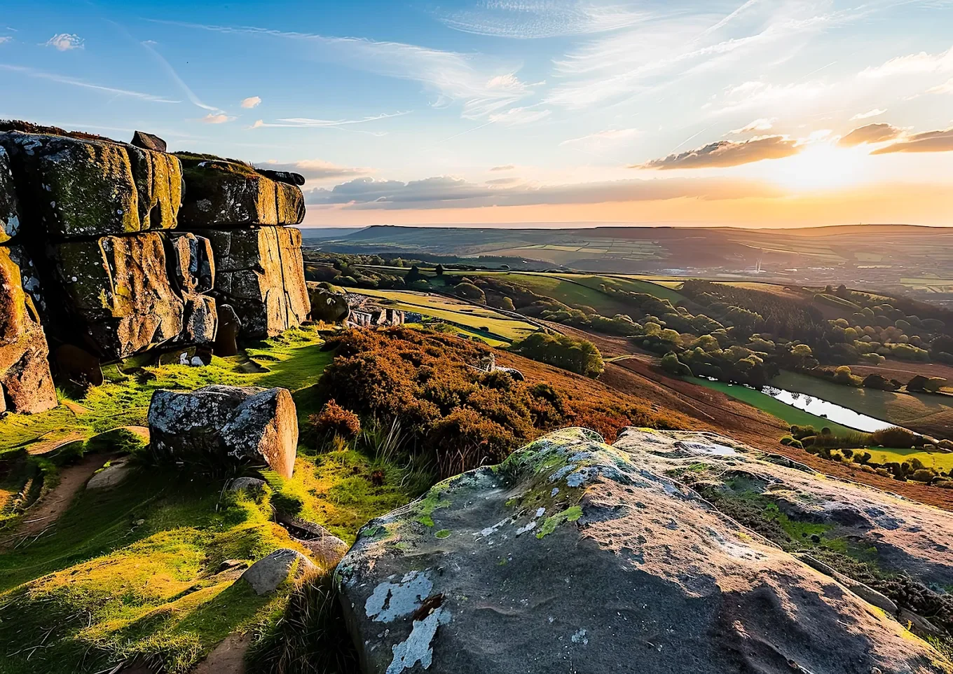 Sunset over rolling hills with large moss-covered rocks in the foreground and a grassy landscape extending into the distance.