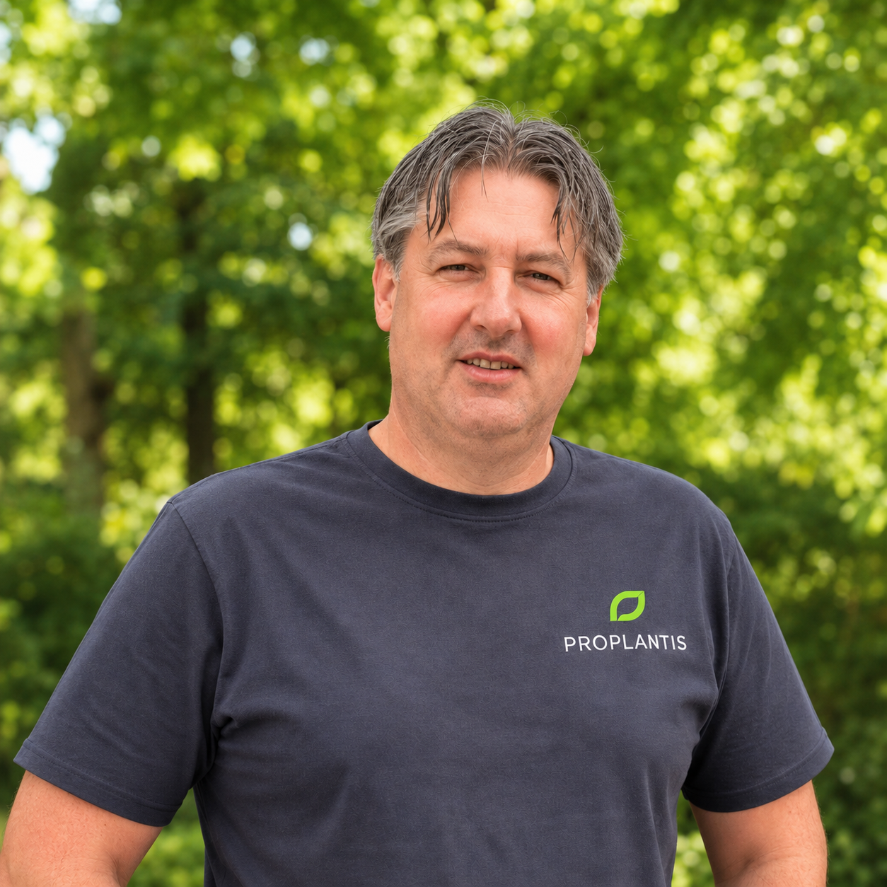 A man in a black t-shirt with a green leaf logo and the word 'PROPLANTIS' on it, standing outdoors with a background of green trees.
