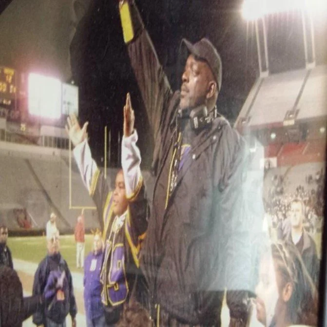 A young football player with a purple uniform celebrating with a handshake or high five with a man in a black jacket at a stadium during nighttime.