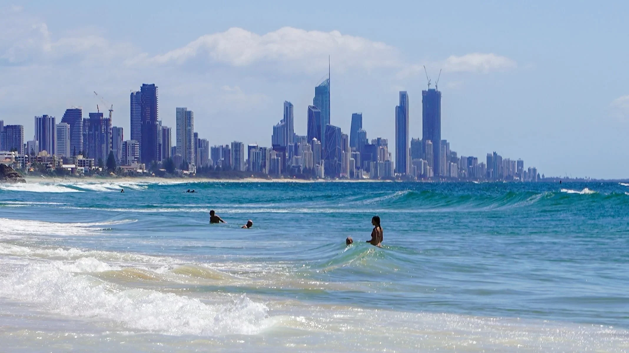 Surfers Paradise w Gold Coast, Australia. Surferzy pływający w oceanie i wysokimi budynkami w oddali. Ilustracja wspomaga sekcję bloga podróżniczego o organizacji podróży do Australii