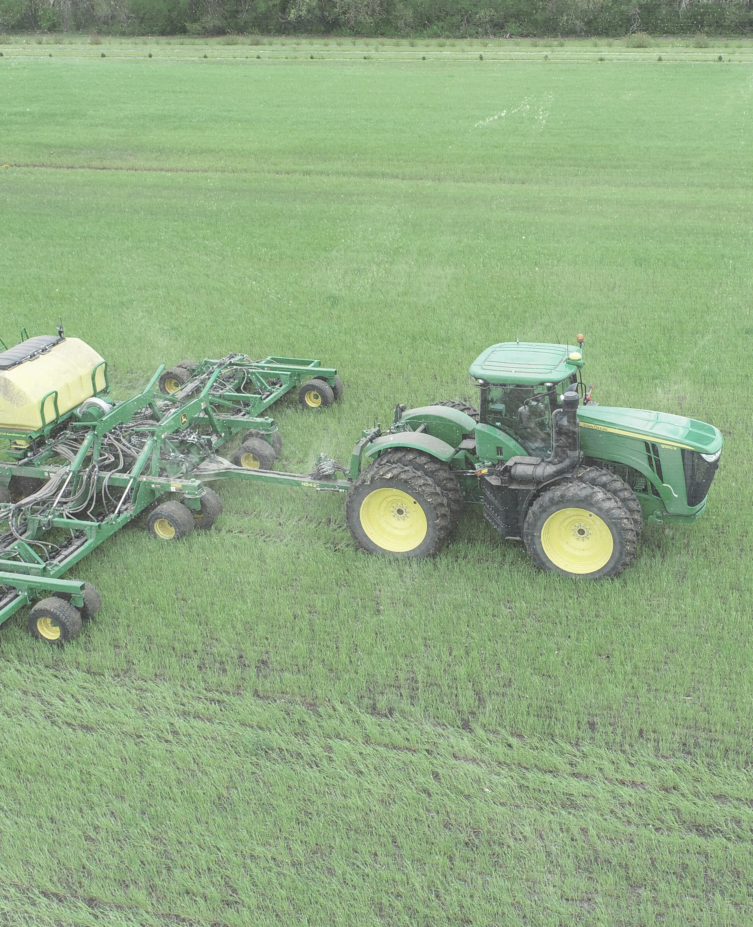 A green tractor pulling agricultural equipment in a green field.