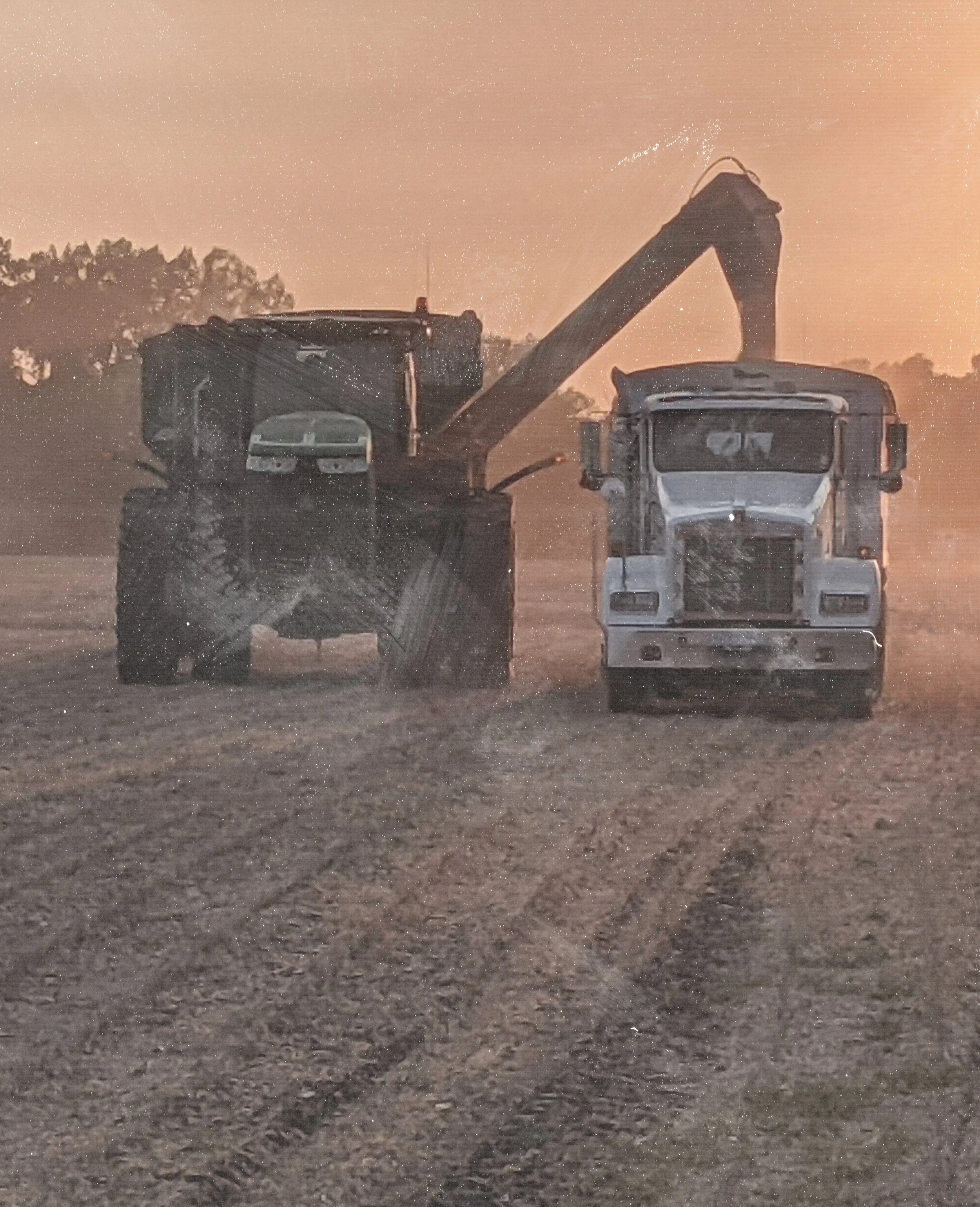 Construction site with a large excavator and a dump truck working at sunset.