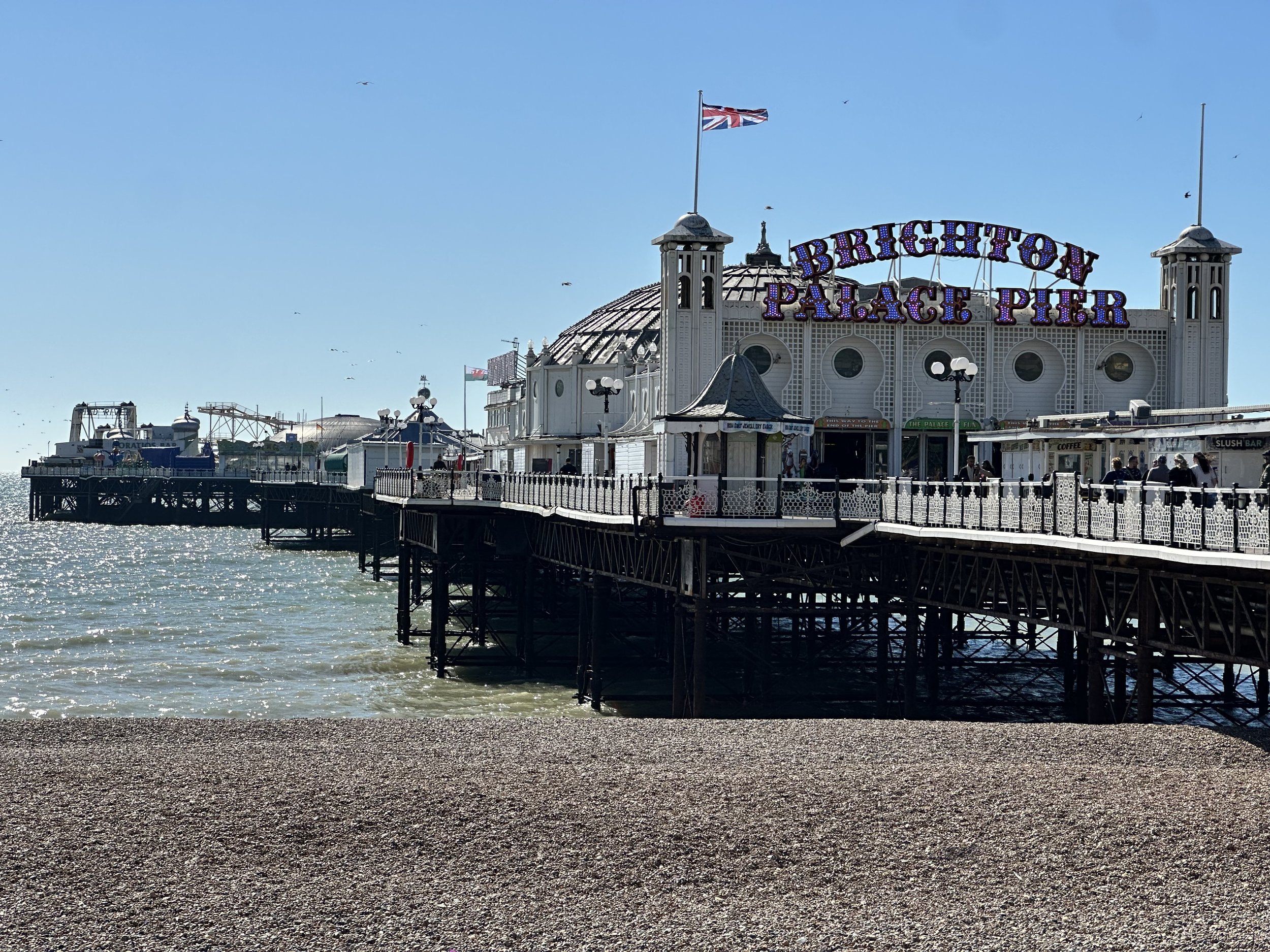The white Victorian structure and signage of Brighton Palace Pier over the sea under a clear blue sky.