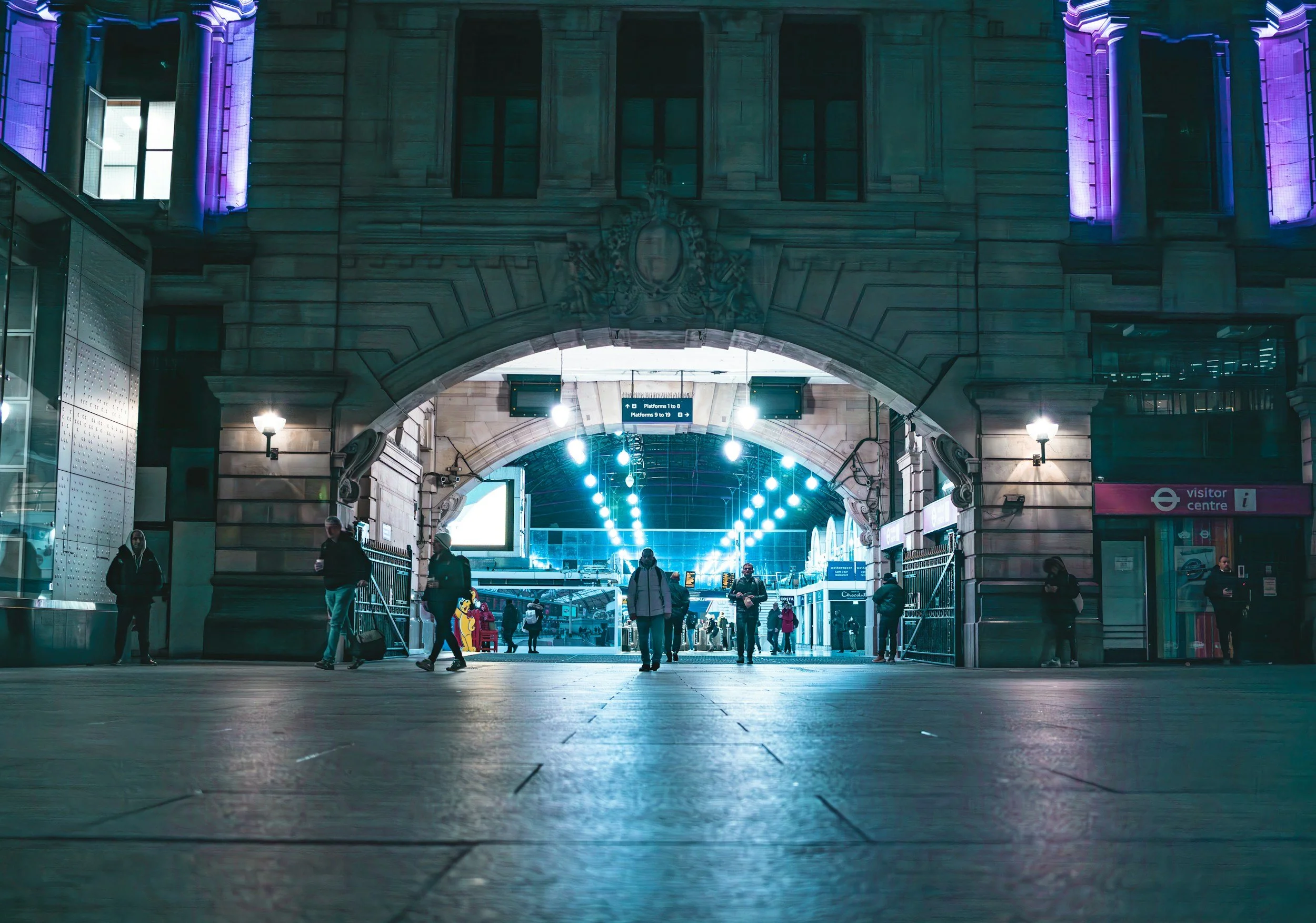 Commuters walking through the stone arch entrance of Victoria Station in London at night.
