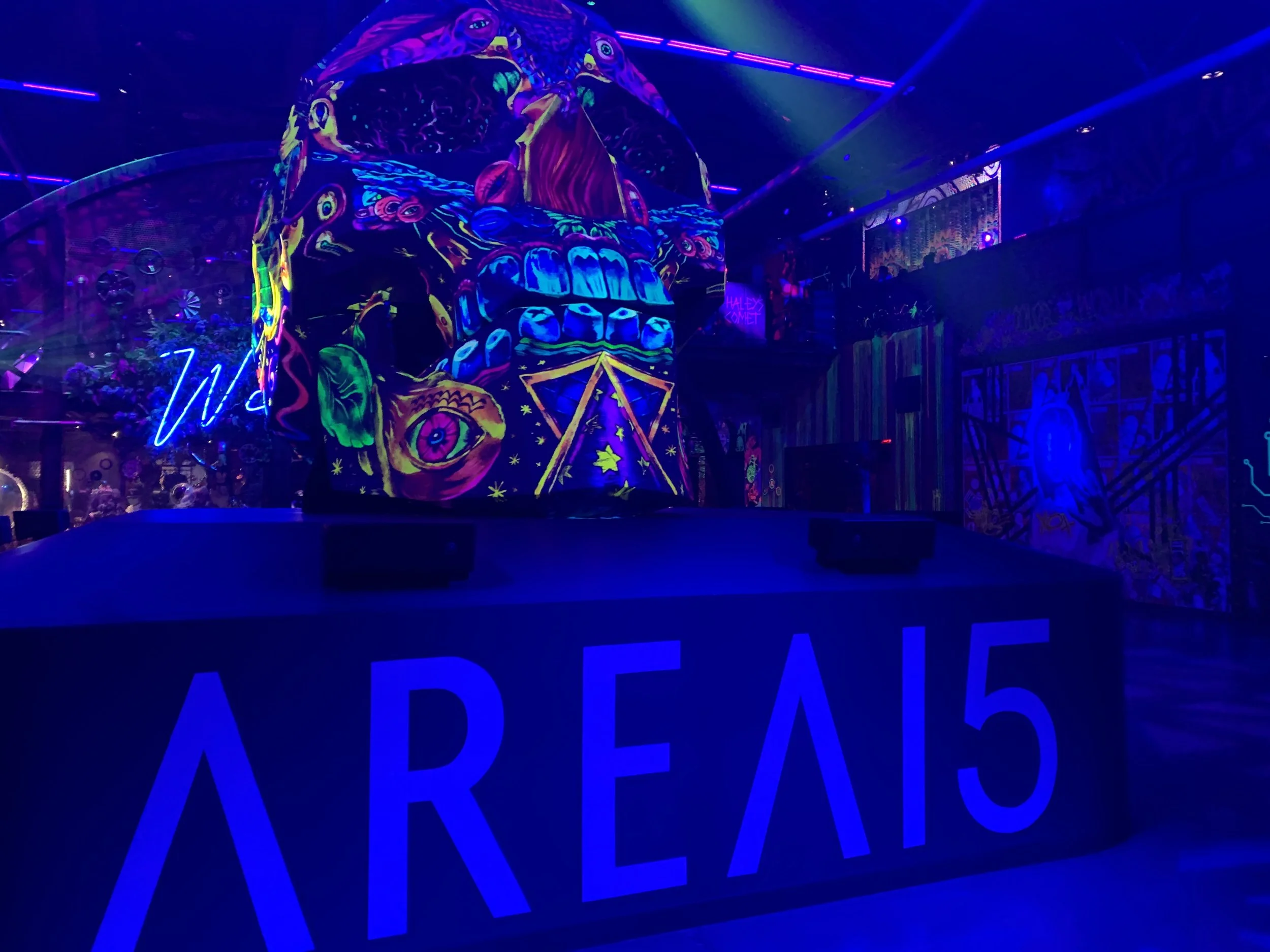 Neon AREA15 sign below a large glowing psychedelic skull art installation in a dark entertainment complex in Las Vegas.