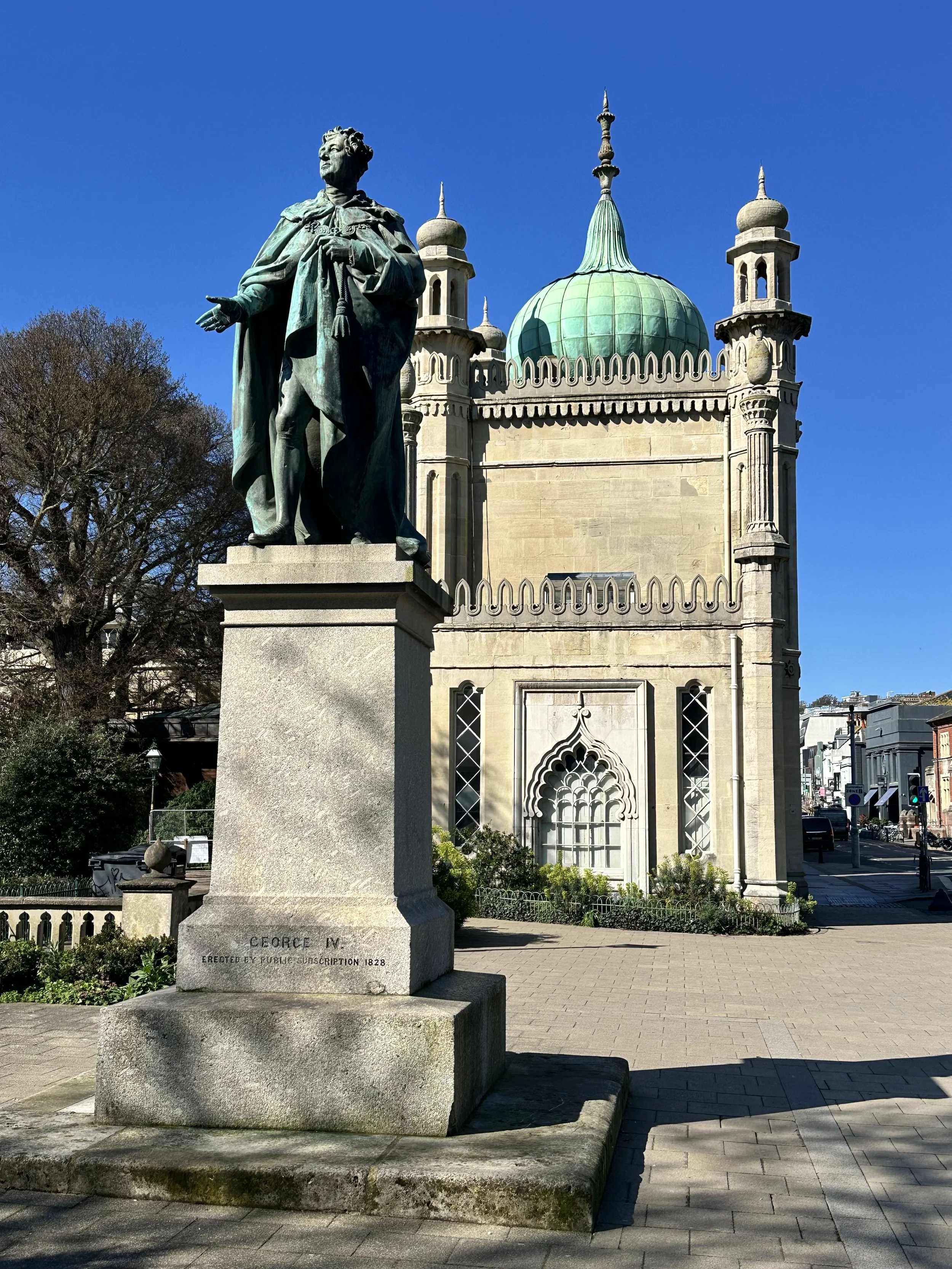 Statue of George IV in front of the Royal Pavilion's onion domes and minarets under a clear blue sky in Brighton.