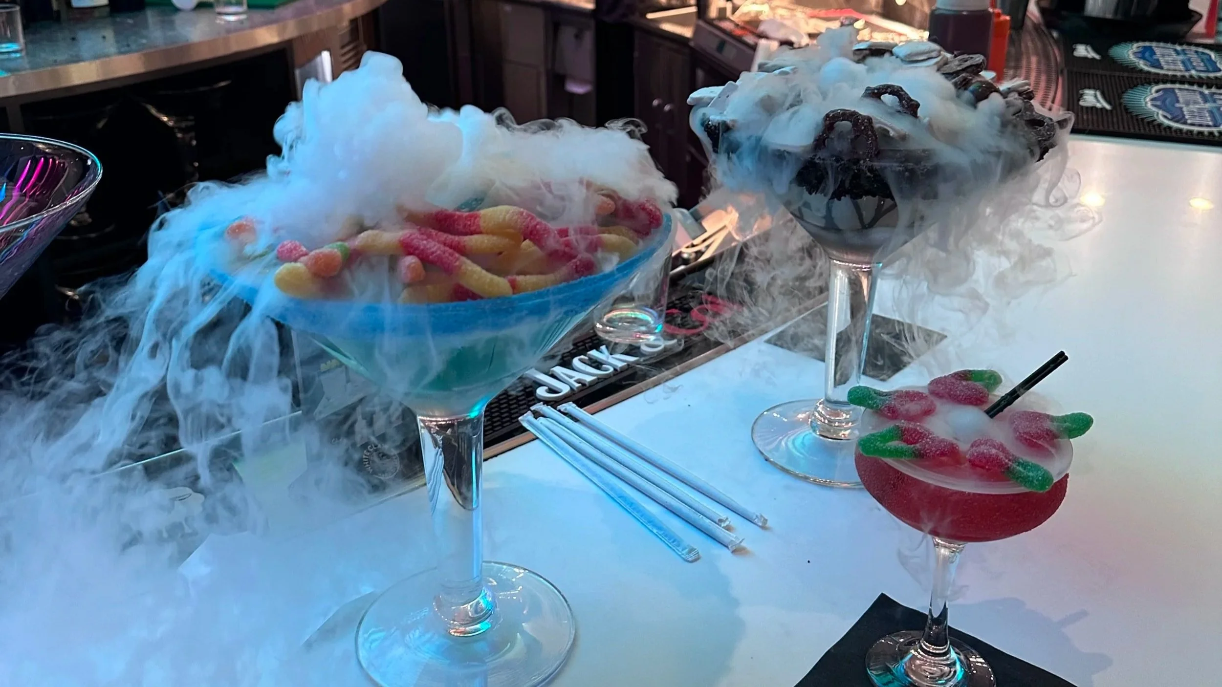 Two large, extravagant nitrogen cocktails at a Las Vegas bar overflowing with white vapor and topped with gummy worm candies and chocolate cookies.