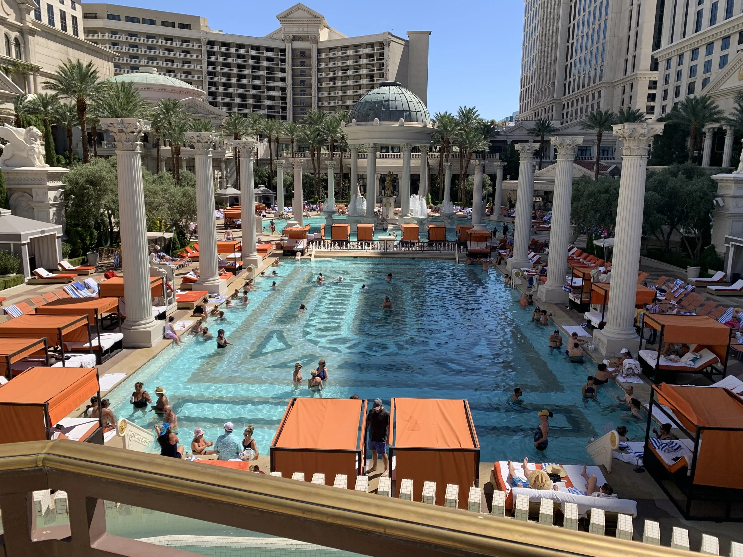 The Garden of the Gods pool at Caesars Palace Las Vegas featuring Roman columns, blue water, and orange cabanas.