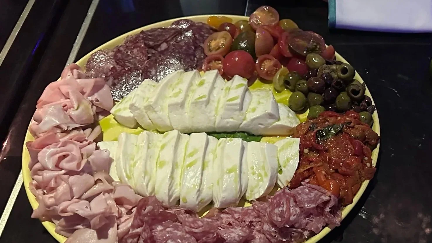 Salami, fresh mozzarella with olive oil, tomatoes, and olives on a yellow plate at Superfrico in The Cosmopolitan Las Vegas.