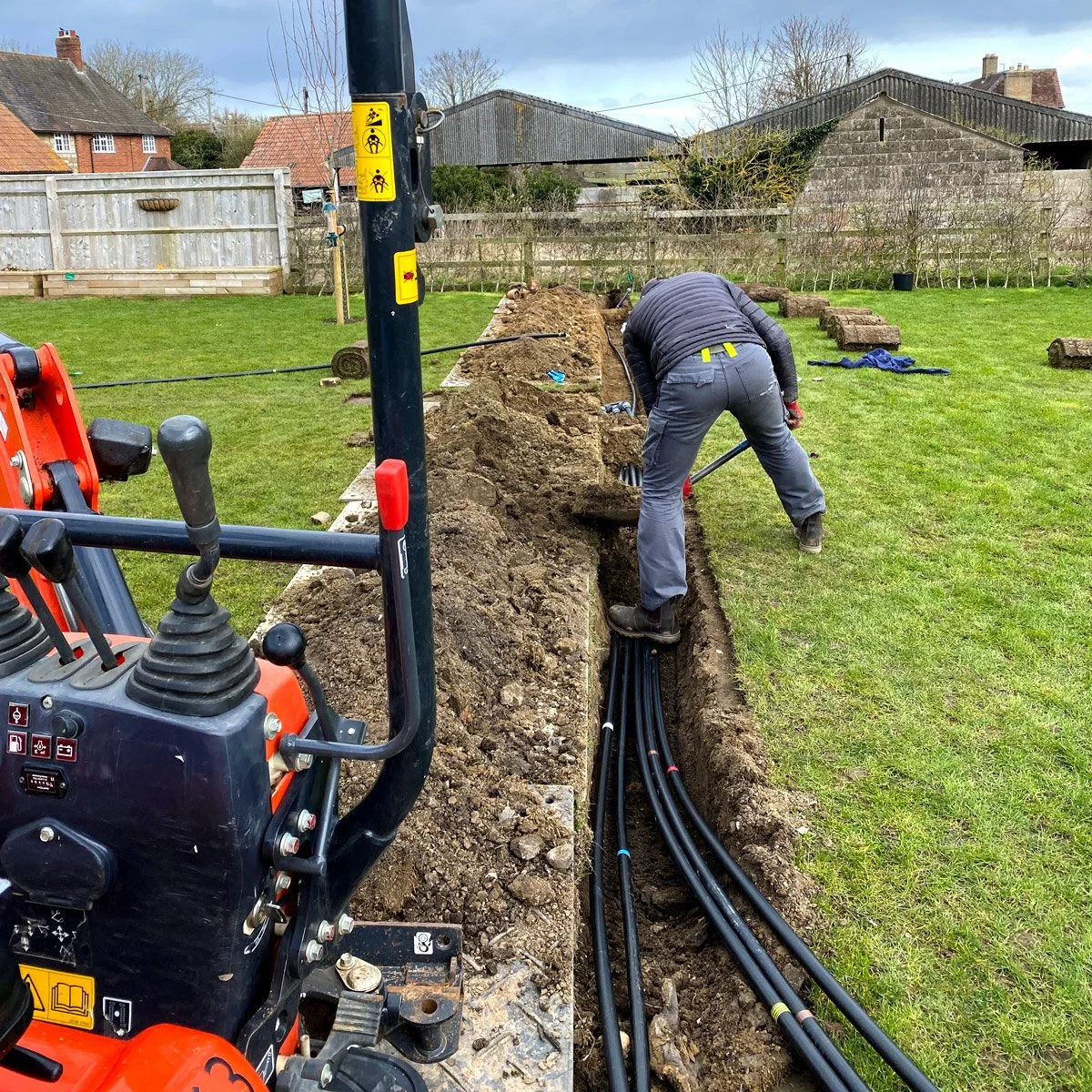 An irrigation specialist from Berkshire worker installing underground pipes in a trench in a backyard, with a small excavator in the foreground.