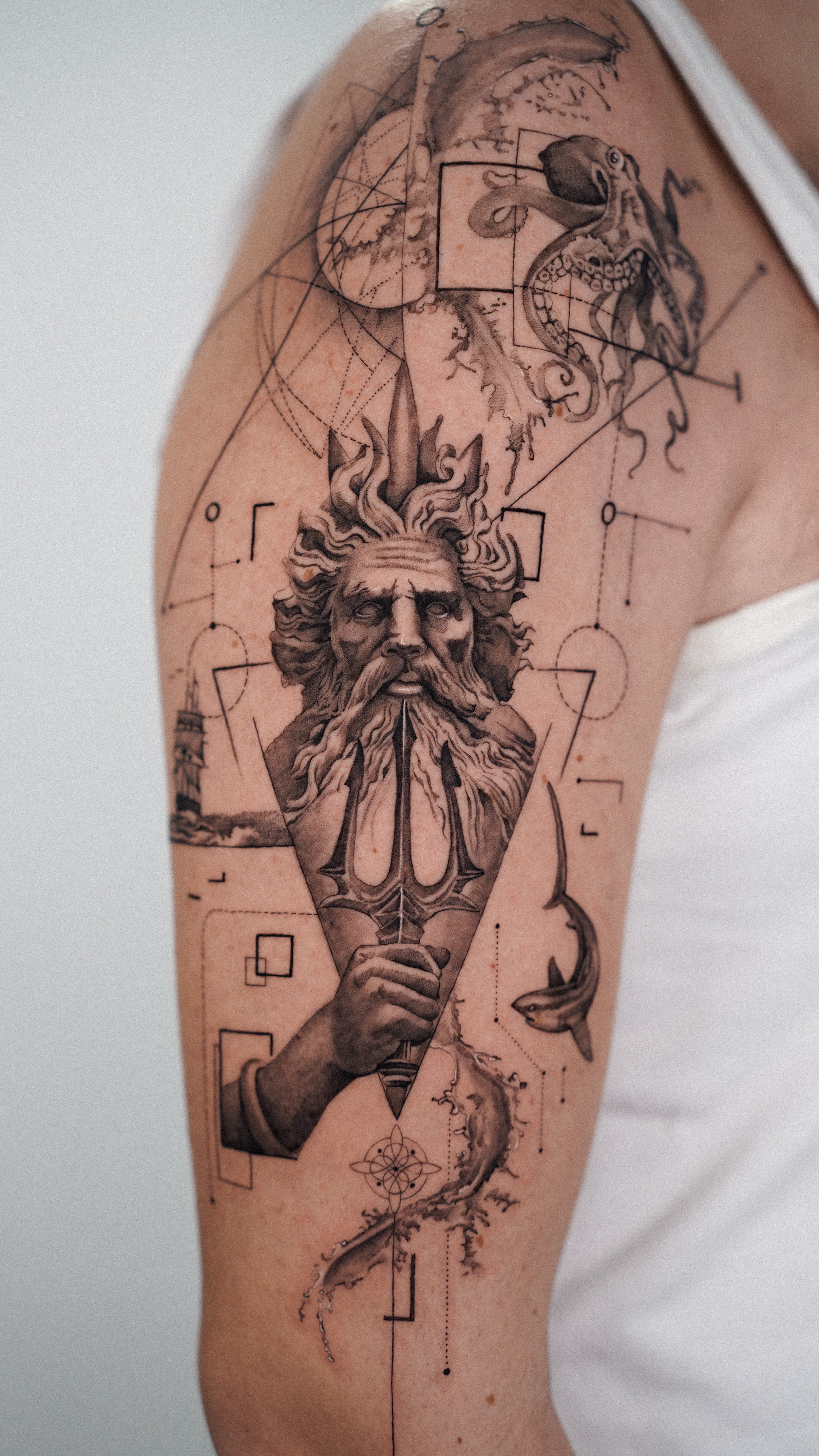 Tattoo of a bearded old man with flowing hair holding a torch, surrounded by geometric and abstract designs on upper arm.