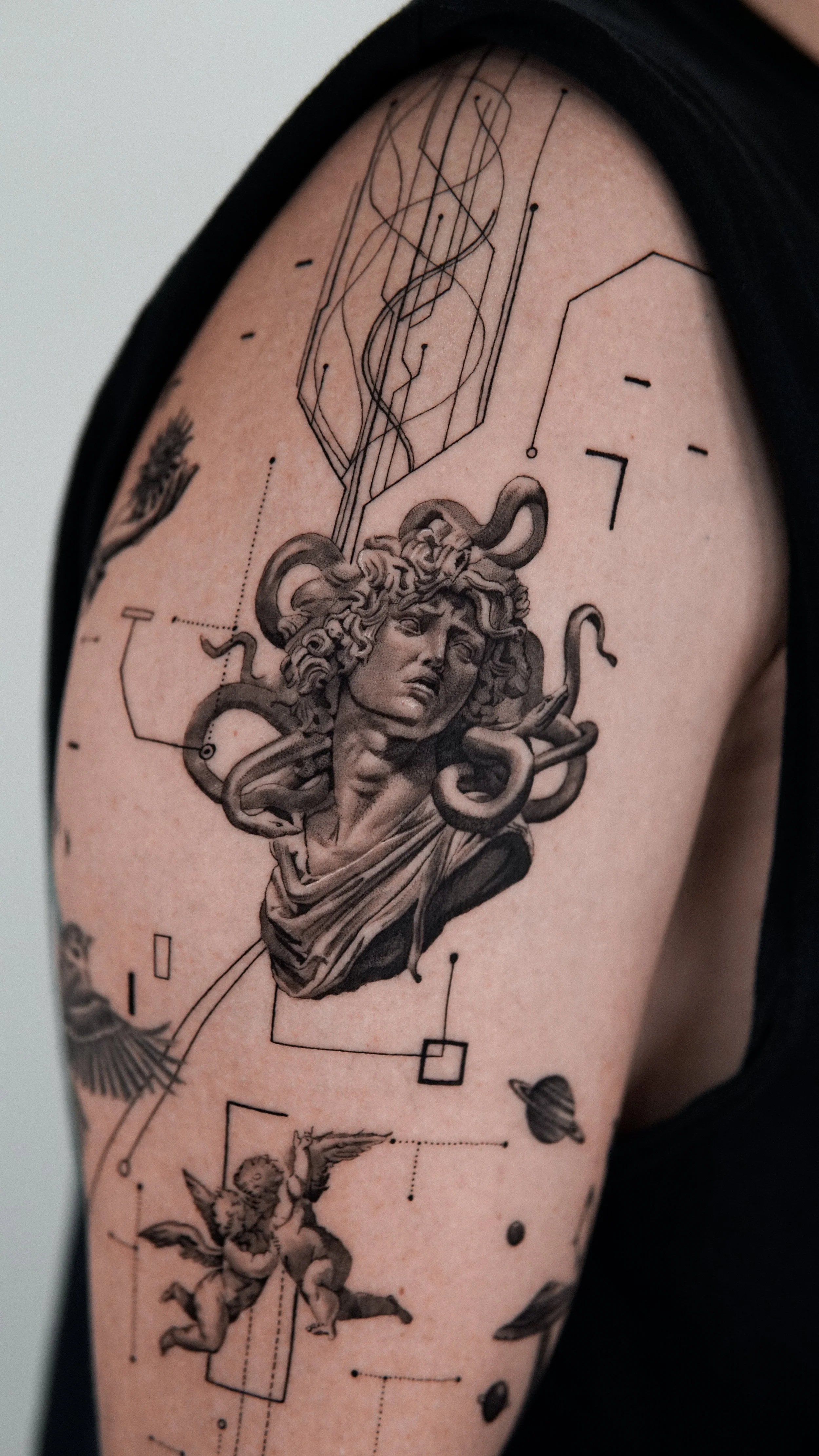 Tattoo of Medusa with snakes for hair, surrounded by geometric and celestial designs, on person's upper arm.