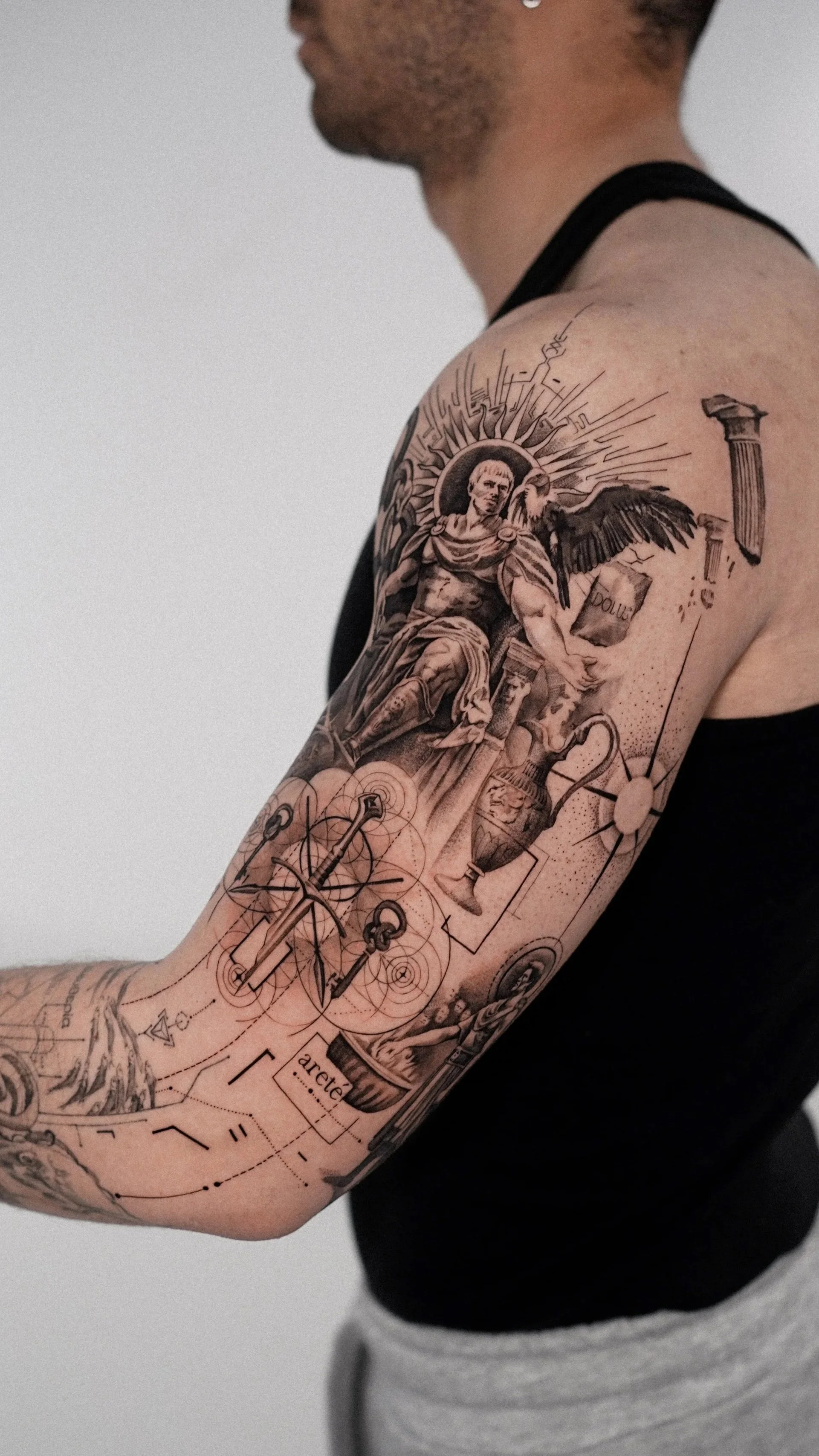 A person with a sleeve tattoo featuring a classical statue, geometric designs, and scientific instruments.