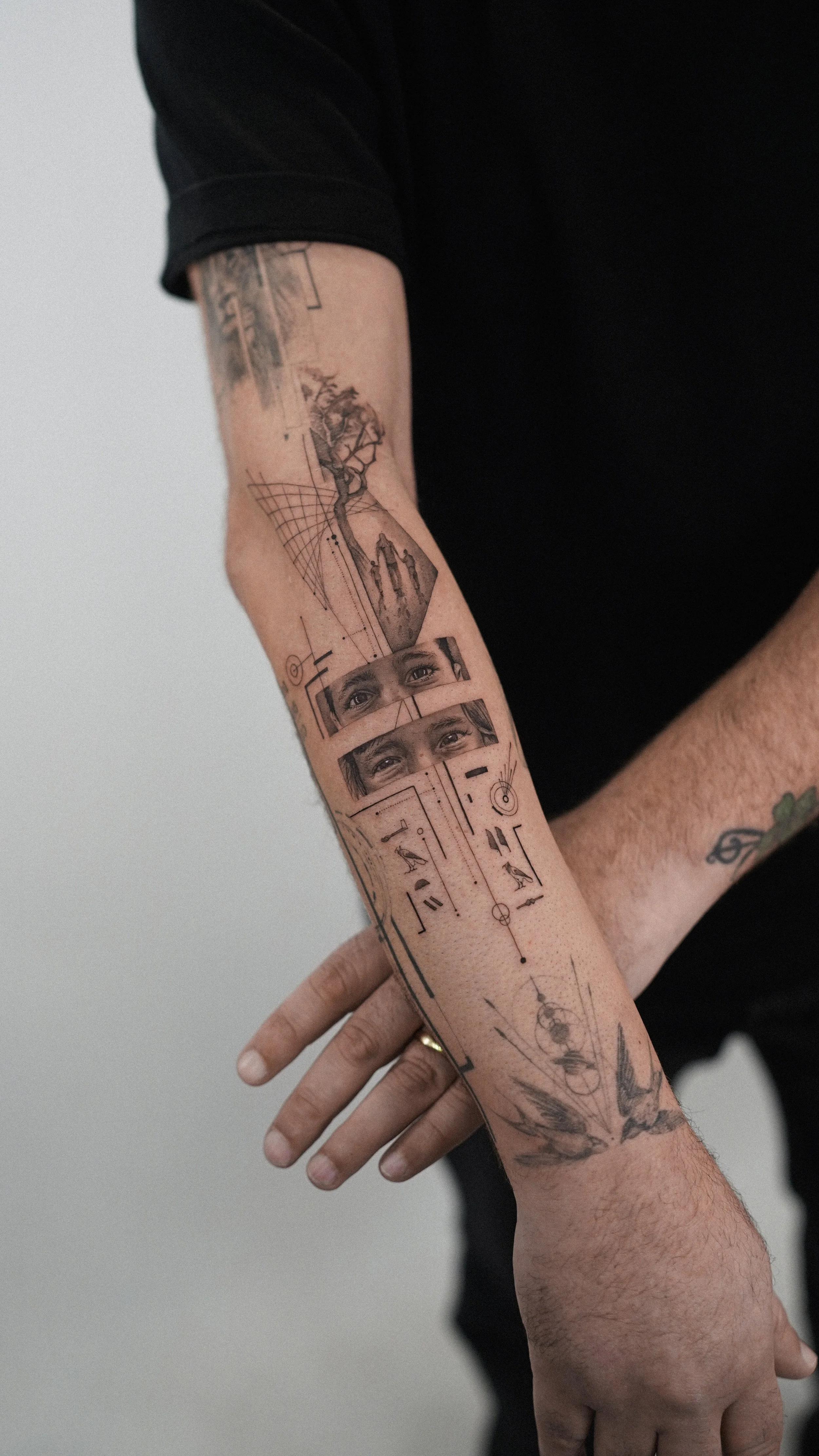 Close-up of a person's arm and hand with a detailed tattoo sleeve consisting of geometric designs, nature scenes, eyes, and abstract elements.