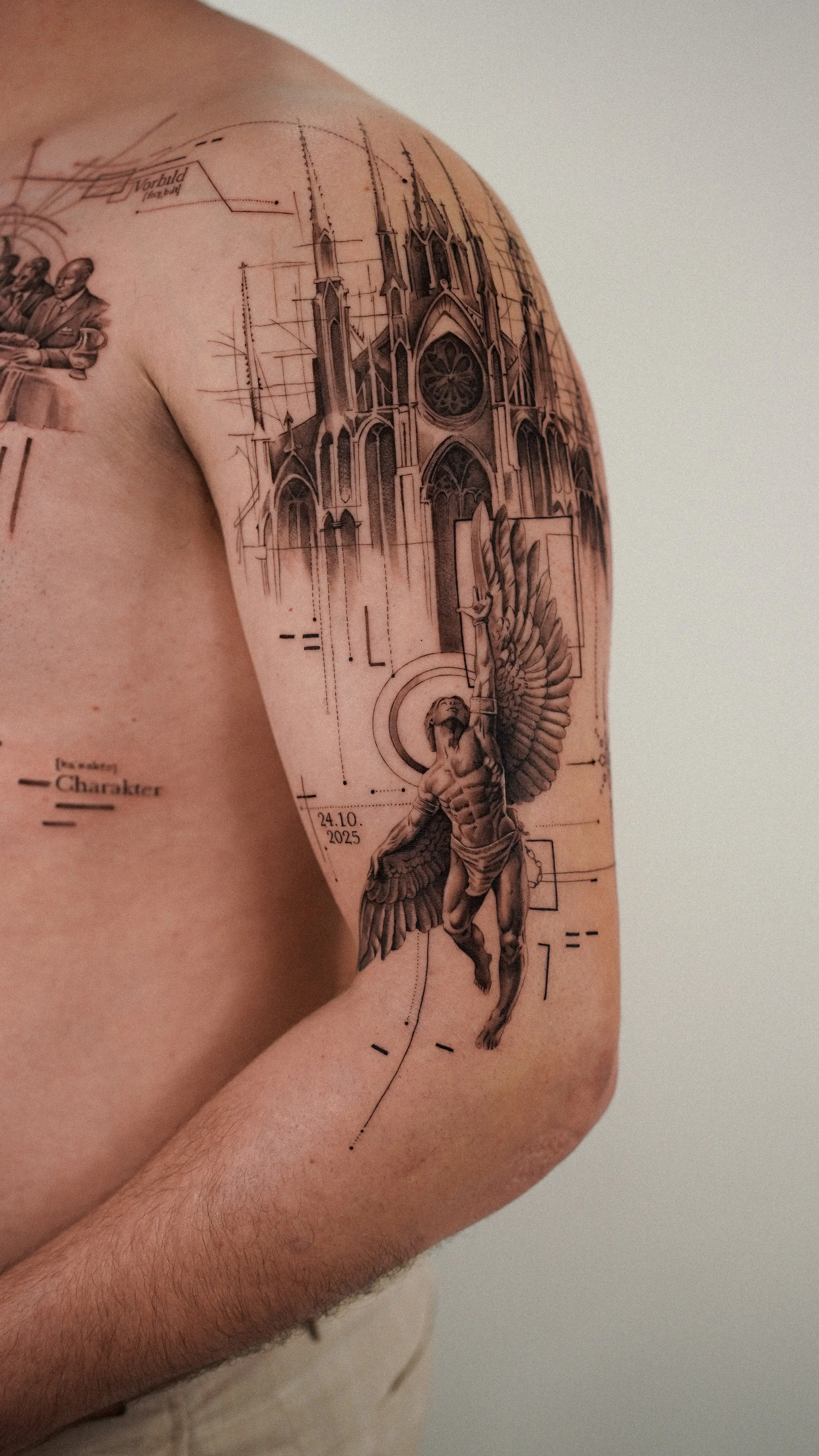 Close-up of a person's shoulder and upper arm tattoo featuring a detailed gothic cathedral skyline, a winged muscular figure with a chain, and various technical drawing elements.