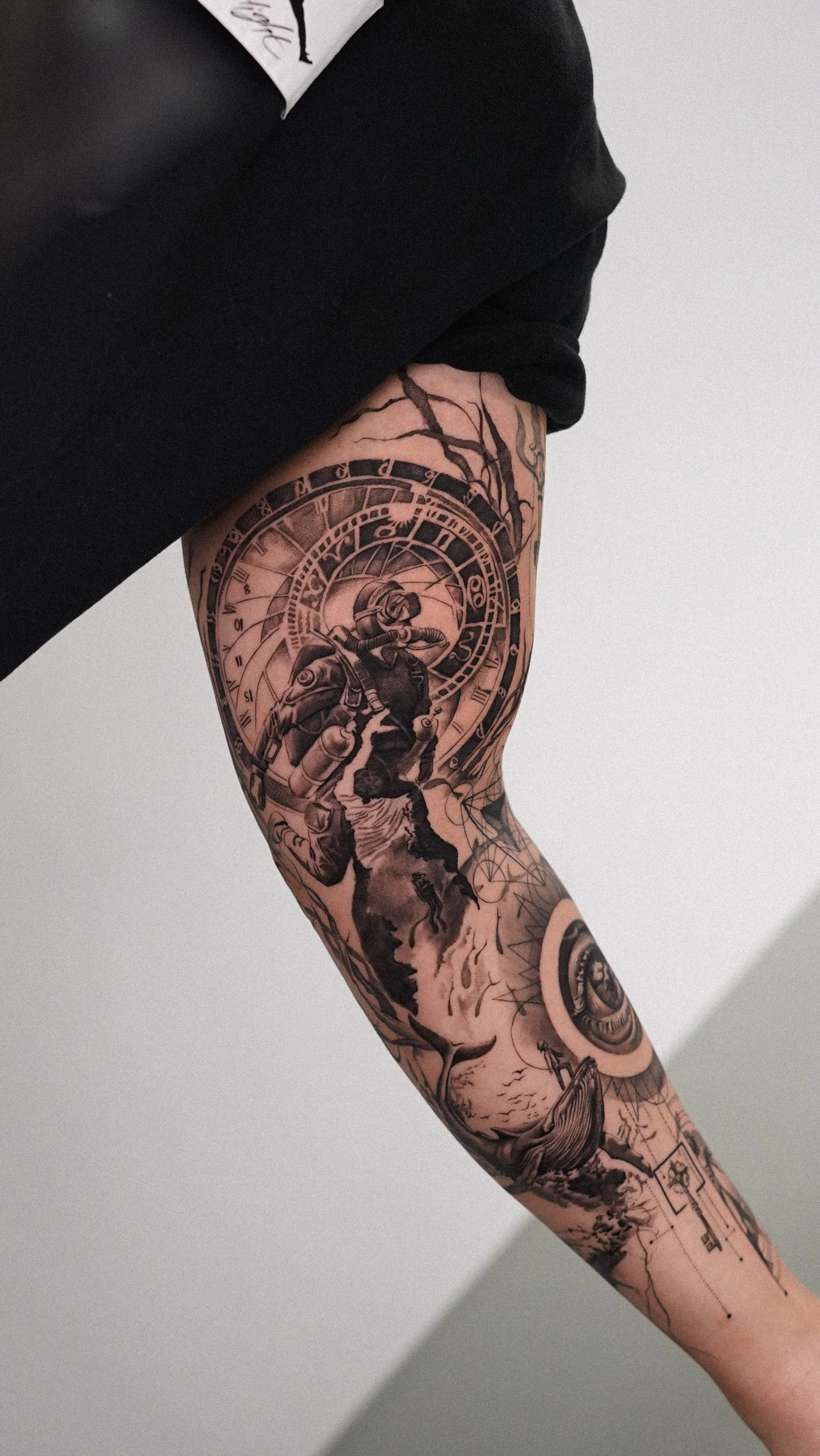 Close-up of a person's tattooed arm and upper thigh, featuring a clock and a soldier on horseback, with other decorative elements.