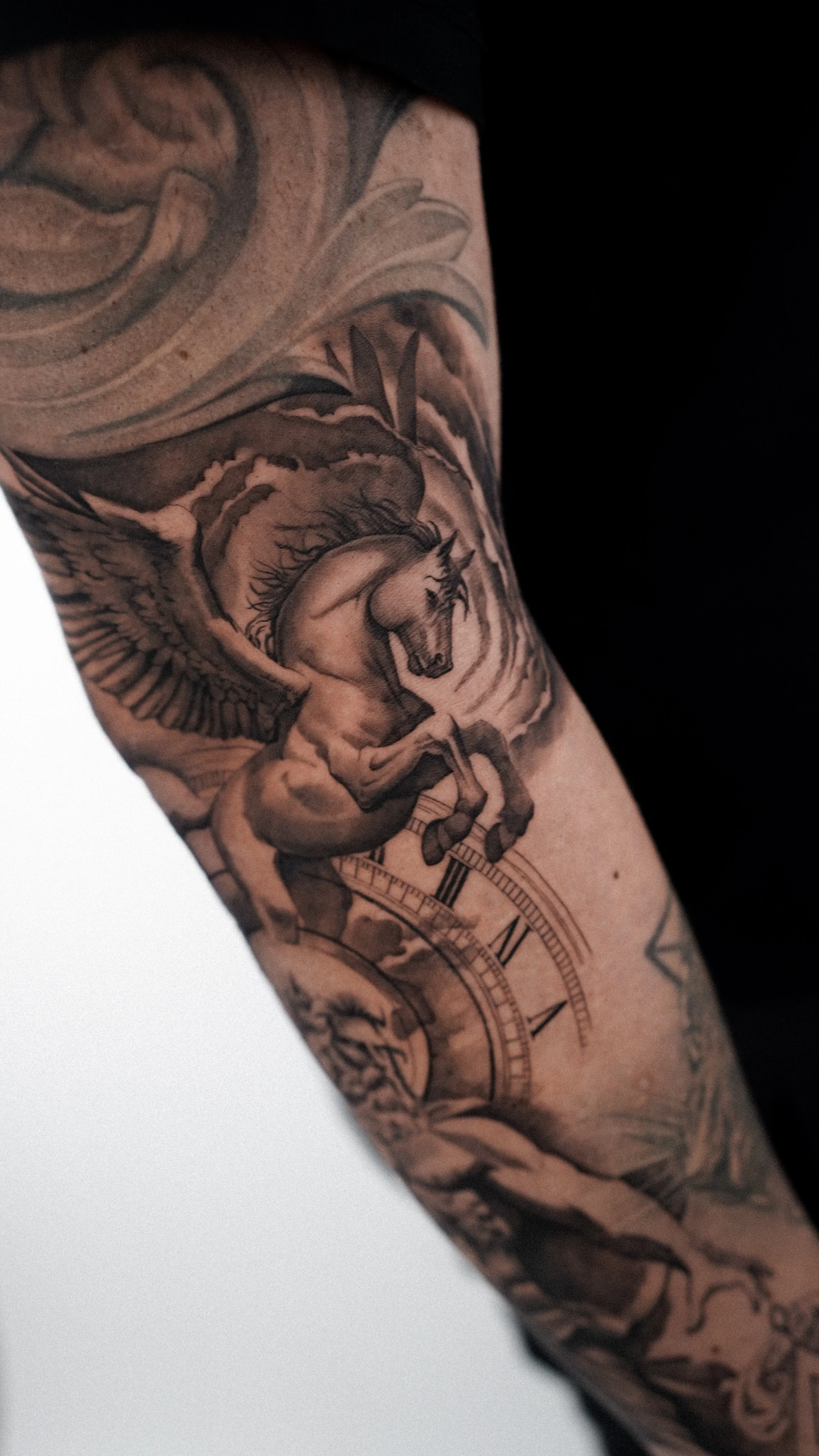 Tattoo of a winged horse with a clock and decorative elements on a person's arm.