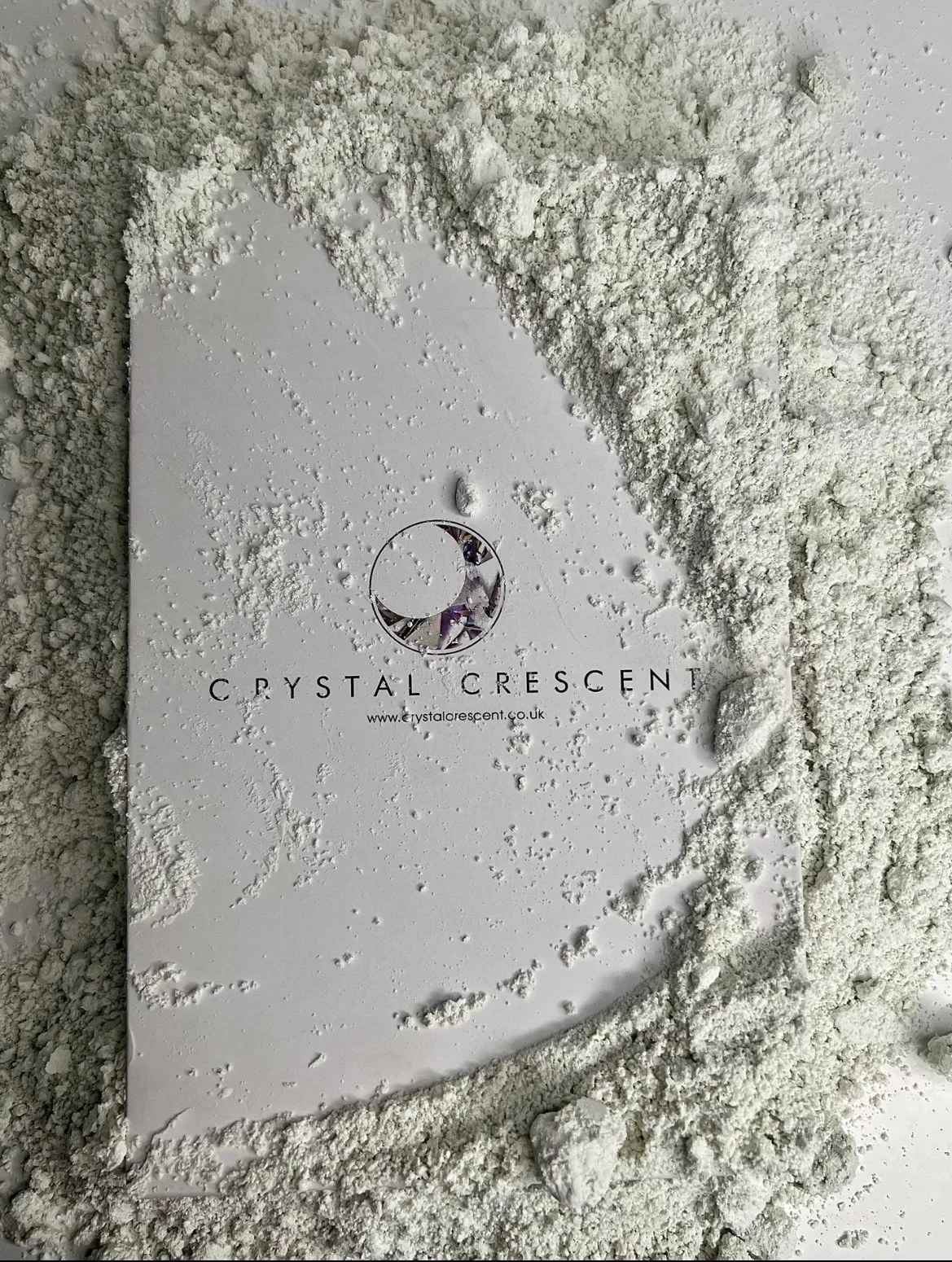 White crystal crescent-shaped box with the logo and website of Crystal Crescent, surrounded by white powder or crushed material.