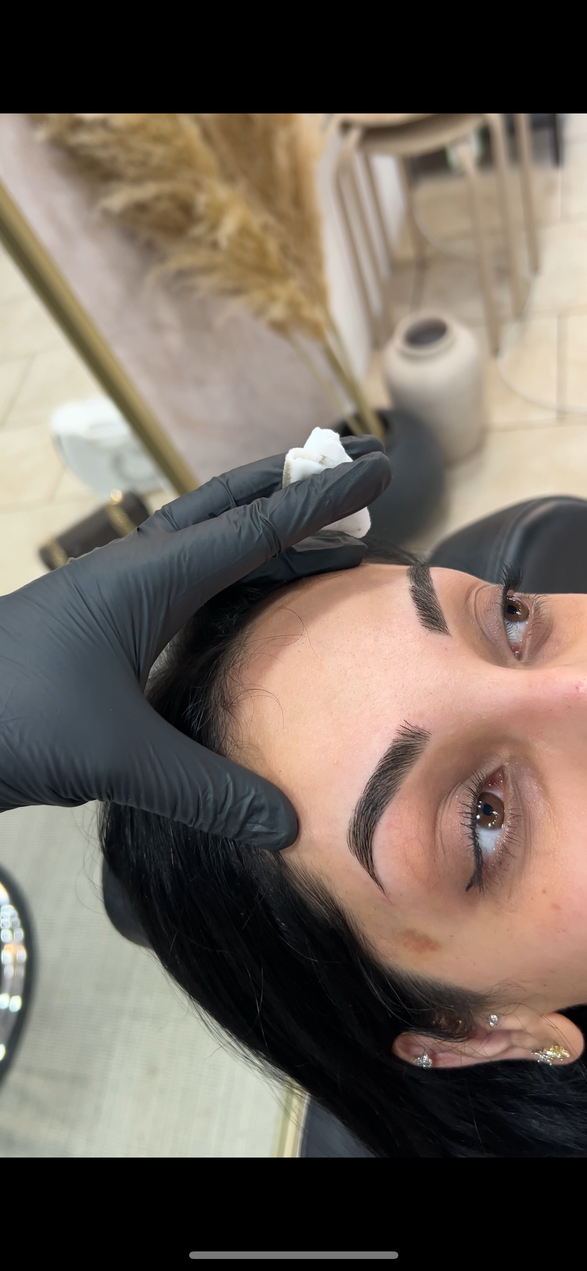 Close-up of a woman receiving an eyebrow treatment at a salon, with a gloved hand gently applying or adjusting her eyebrows.