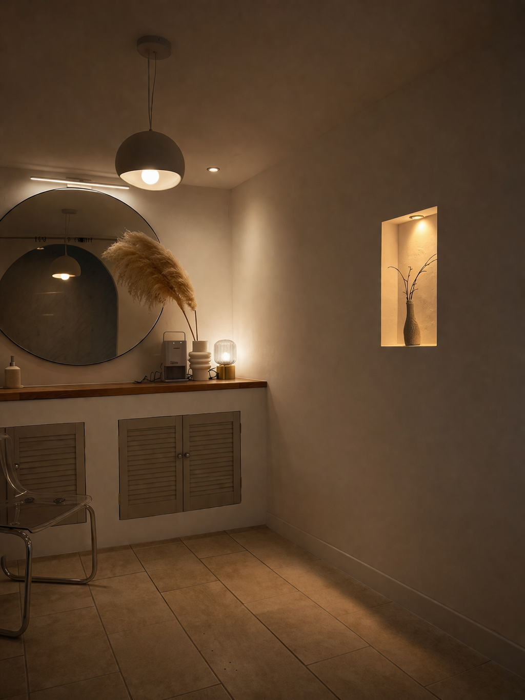 A cozy, dimly lit interior with a round mirror, a small table with decorative items, including a lamp and dried pampas grass, a transparent chair, and a wall niche with a vase and minimal decor. a room by crystal crescent