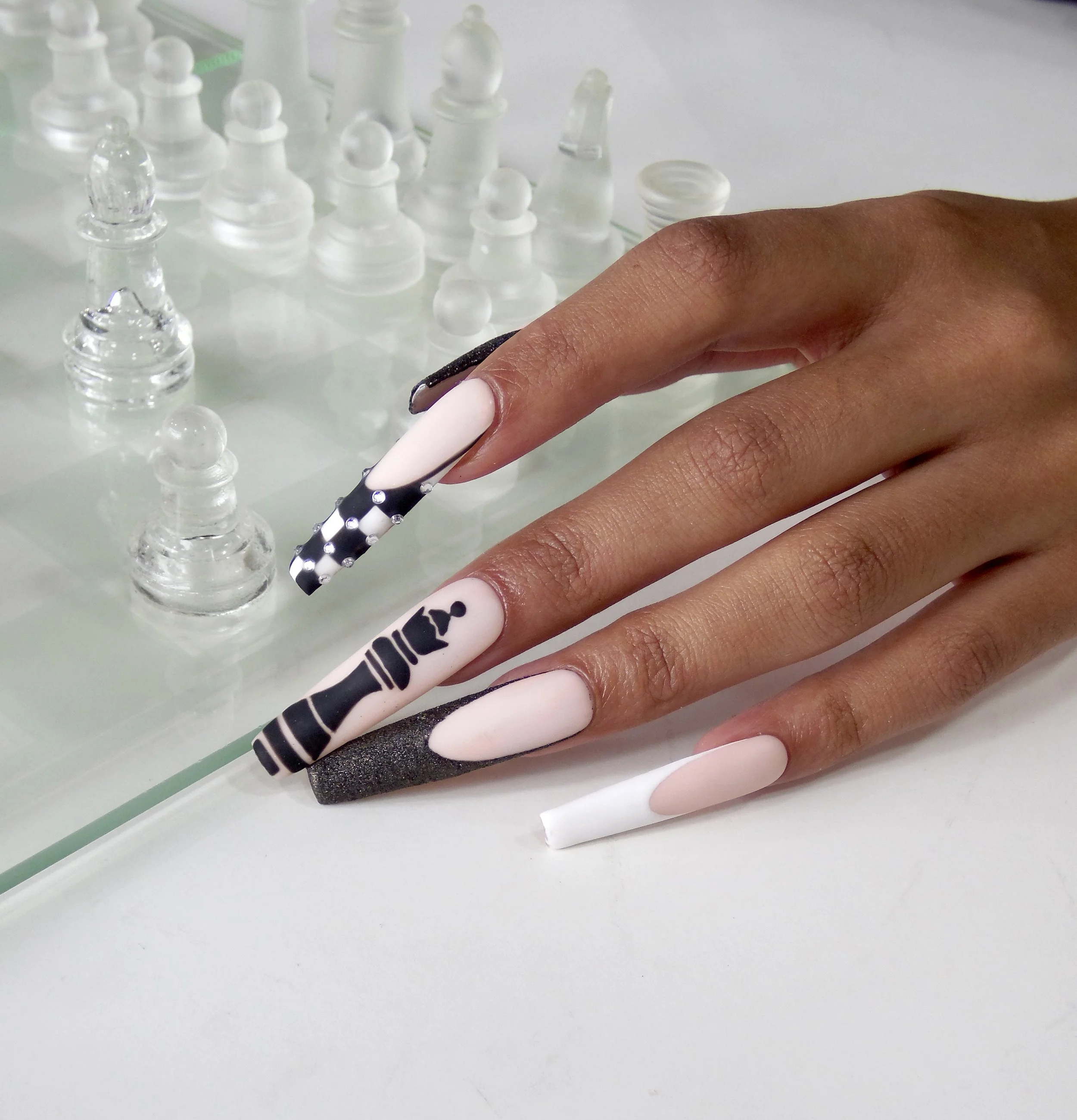 Person with decorated acrylic nails applying nail polish at a table with a chess set.