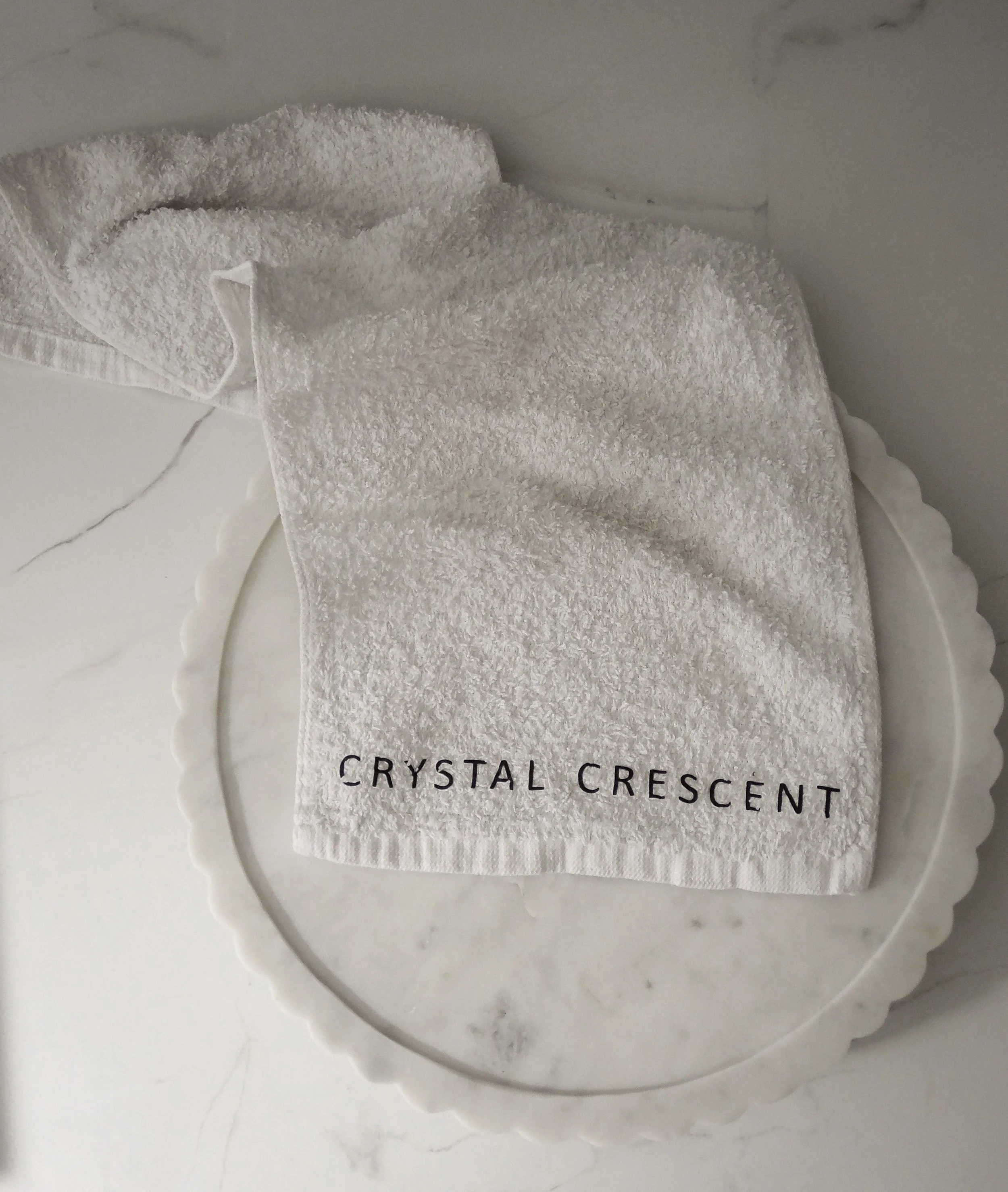 A white towel with the text 'CRYSTAL CRESCENT' embroidered on it in black, placed on a white marble surface.