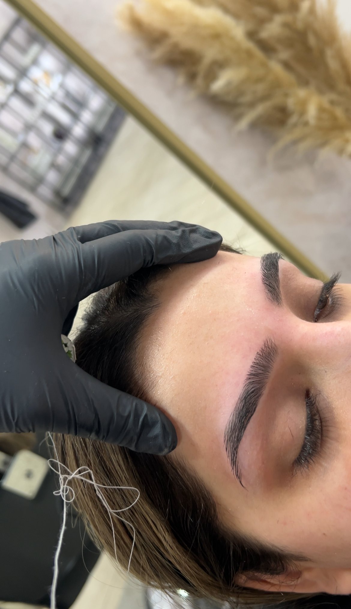 Close-up of a woman with freshly done eyebrow threading, receiving touch-up, in a salon or clinic environment.