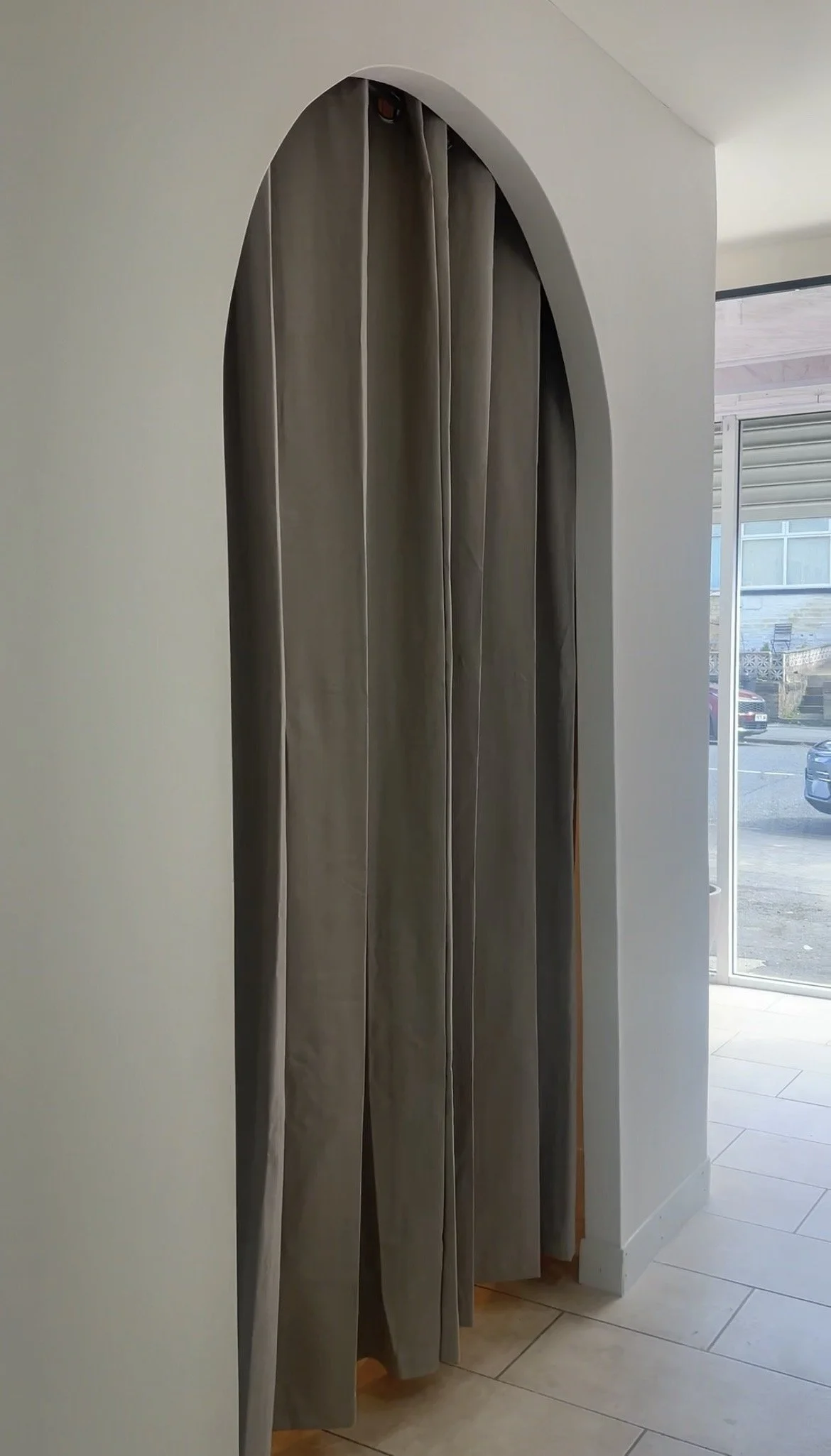 Gray curtains hanging in a doorway with a view of a room and parking lot outside through sliding glass doors.