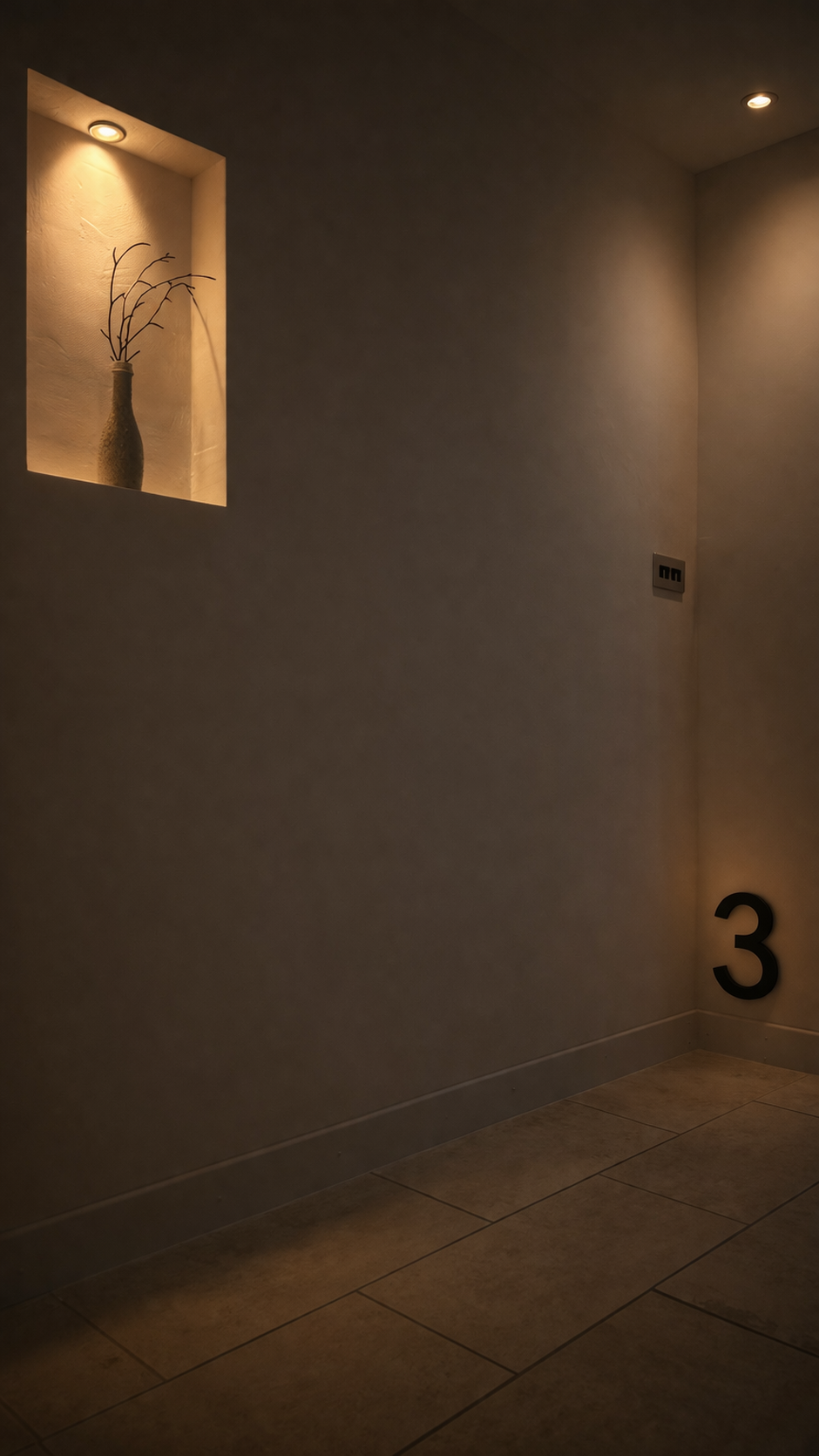 A dimly lit corner of a room with two recessed ceiling lights, a small wall niche with a lit background, a decorative vase with branches, and a large black number 3 on the lower right corner of the wall.
