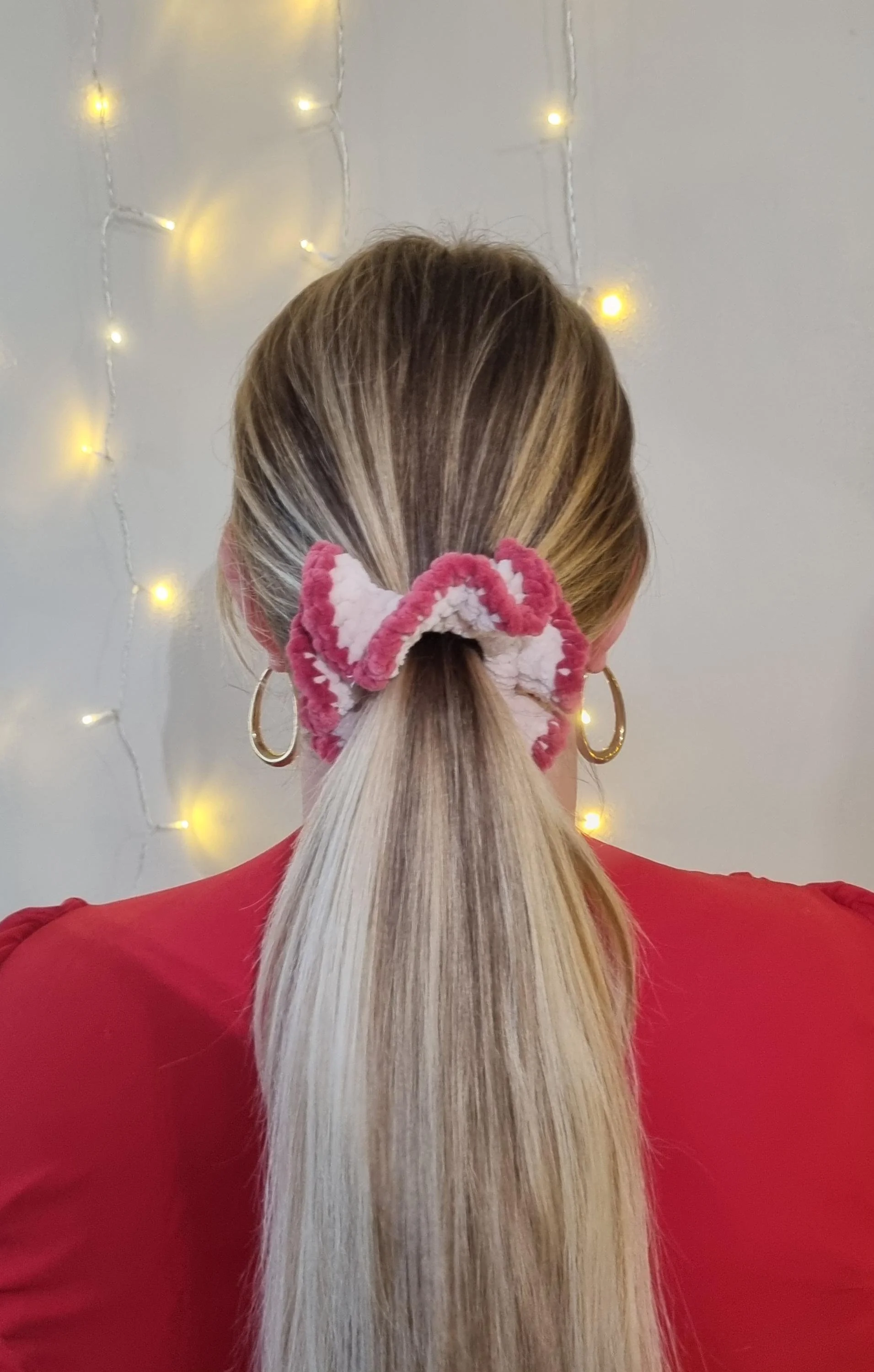 Photo d'une personne vue de dos portant une queue-de-cheval avec un large chouchou crocheté en forme de nœud en tissu à motifs roses et blancs.