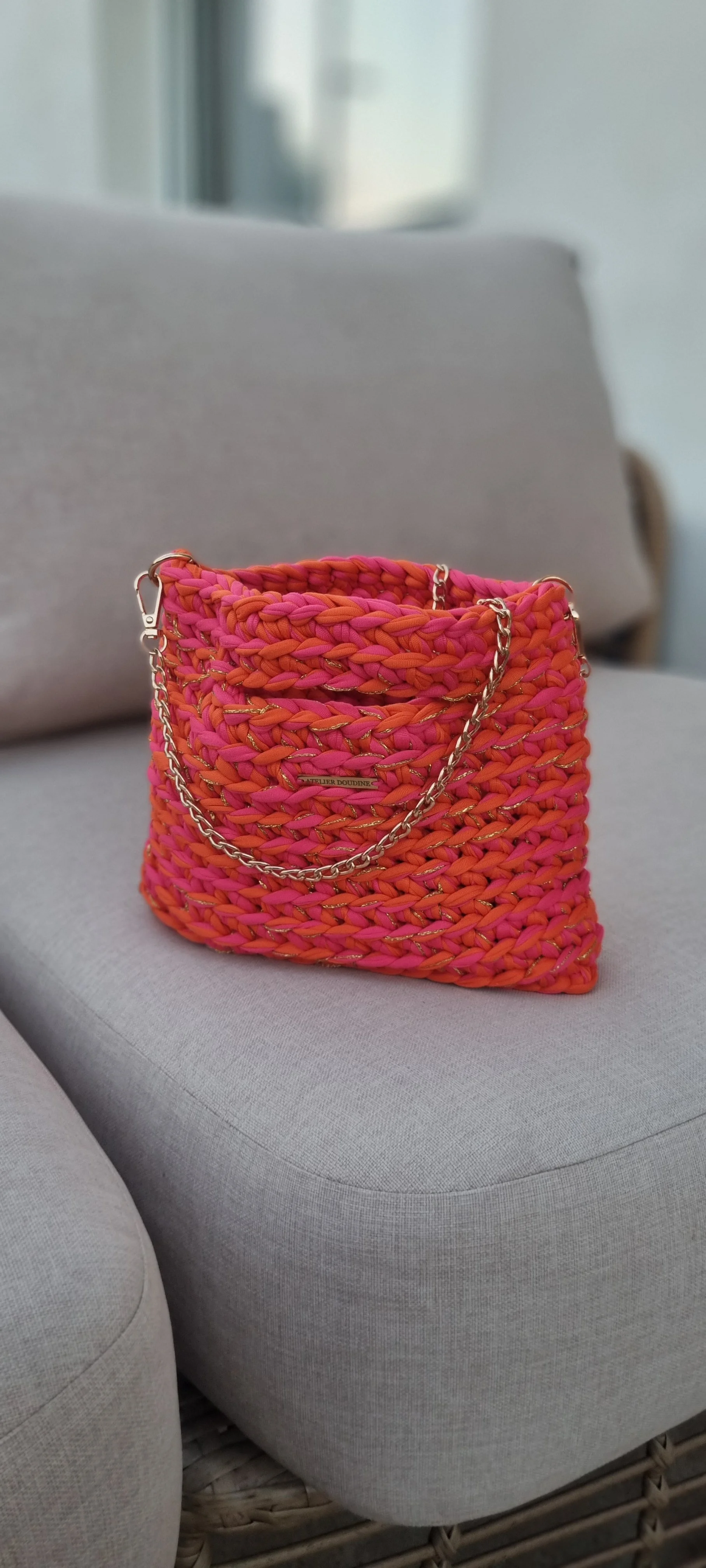 Sac à main crocheté de couleur marron avec chaîne en or, posé devant un canapé en tissu beige.