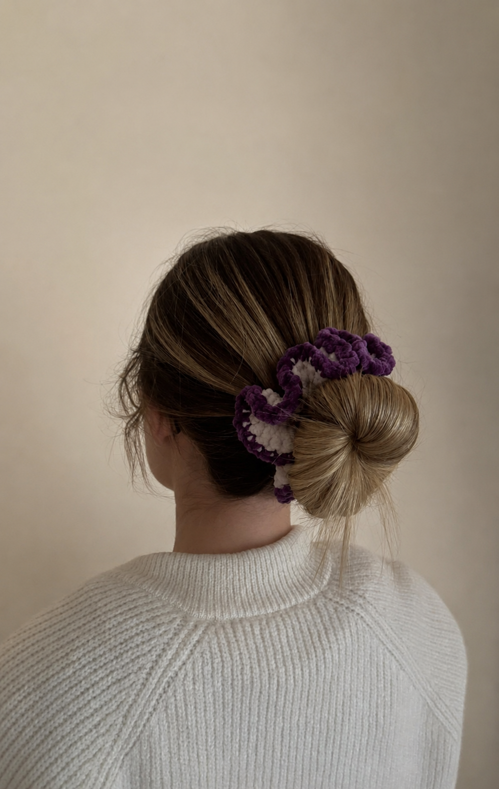 Photo d'une personne vue de dos portant une queue-de-cheval avec un large chouchou crocheté en forme de nœud en tissu à motifs roses et blancs.