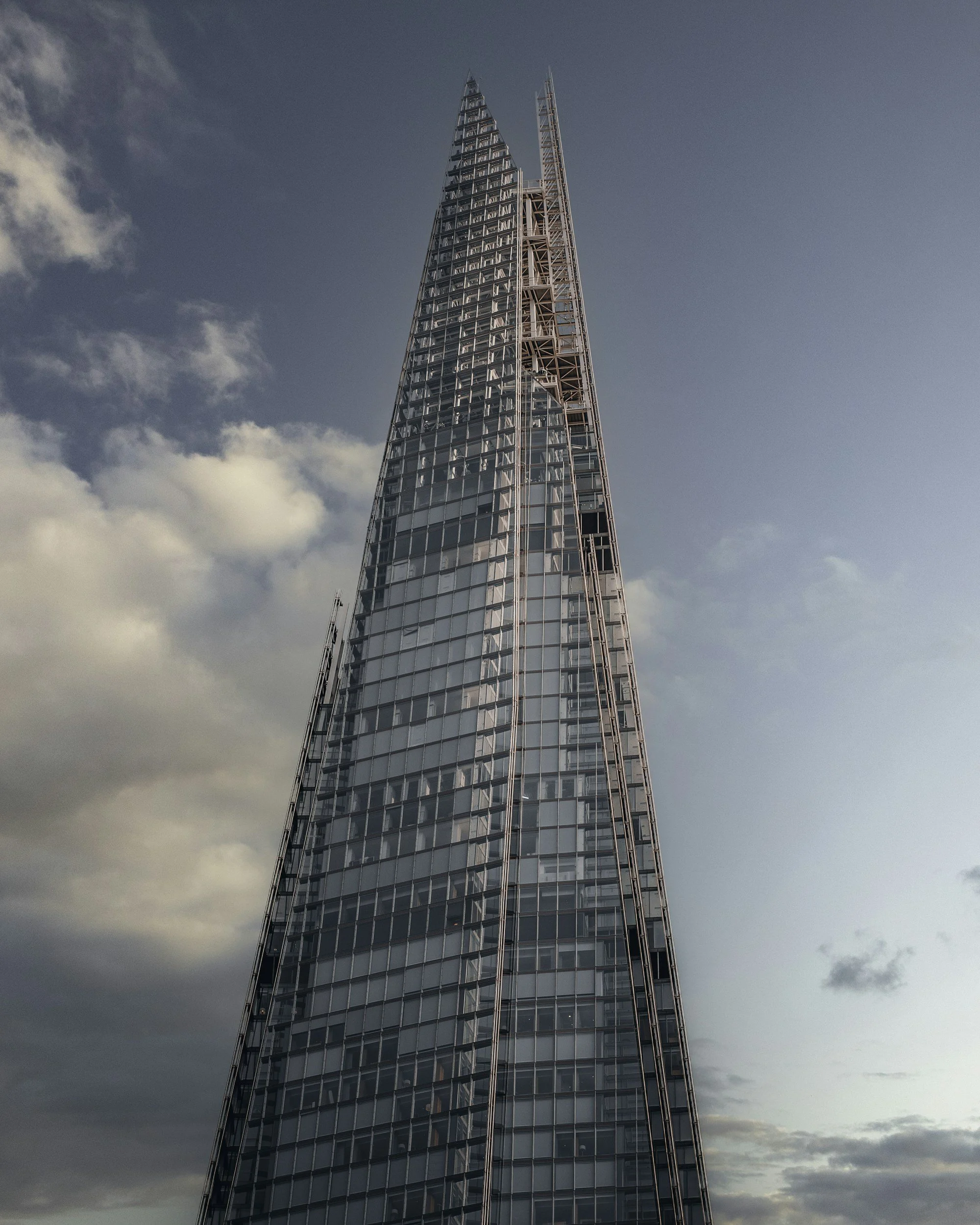 A tall modern glass skyscraper with a pointed top under a cloudy sky.