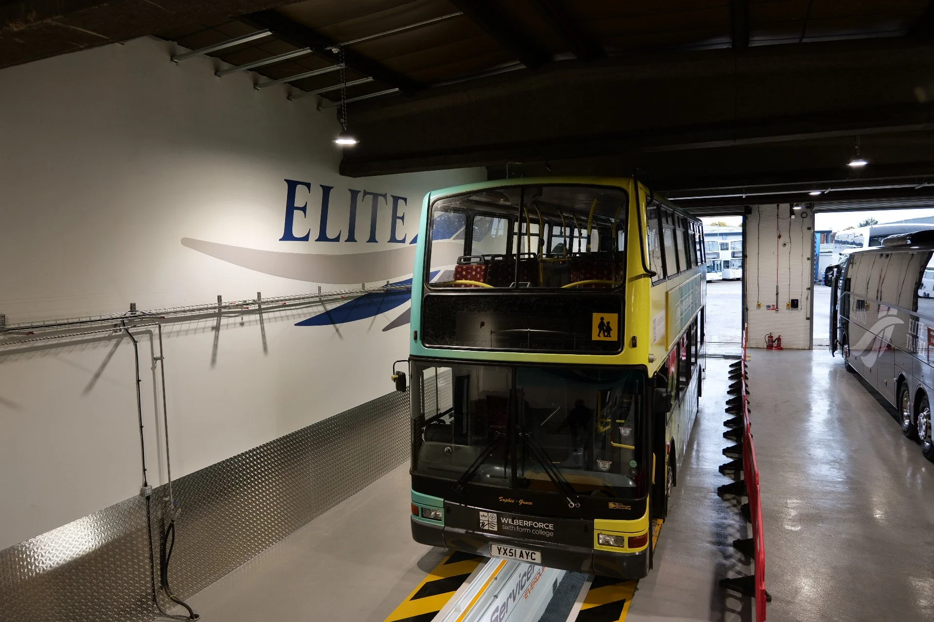 Double-decker bus parked inside a building with a wall mural of the word 'ELITE' and a swoosh logo