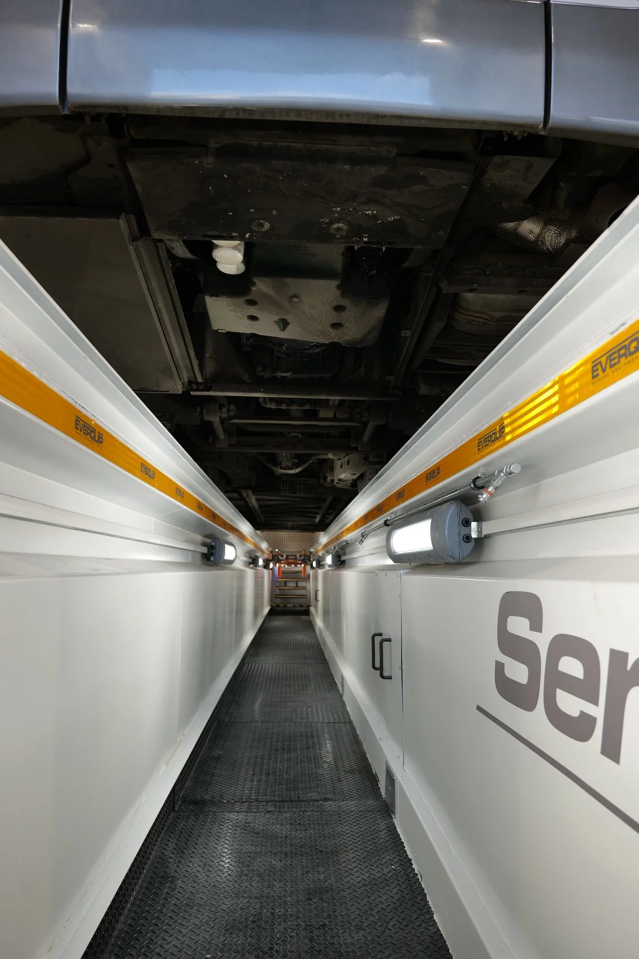 Underbody view of a vehicle on a vehicle inspection or service platform with white sides, black rubber mat floor, and yellow edging labeled 'Everclip.'