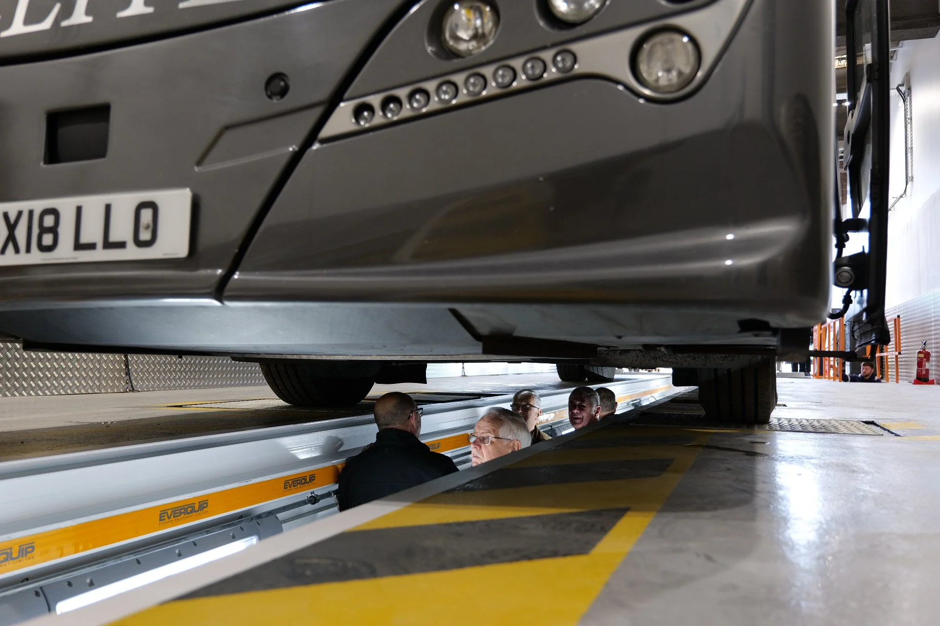 Interior of an industrial space with a large, colorful wall mural featuring various graphic designs, text, and vintage images, with hanging rectangular panels in green, blue, and pink overhead, and an empty concrete floor.