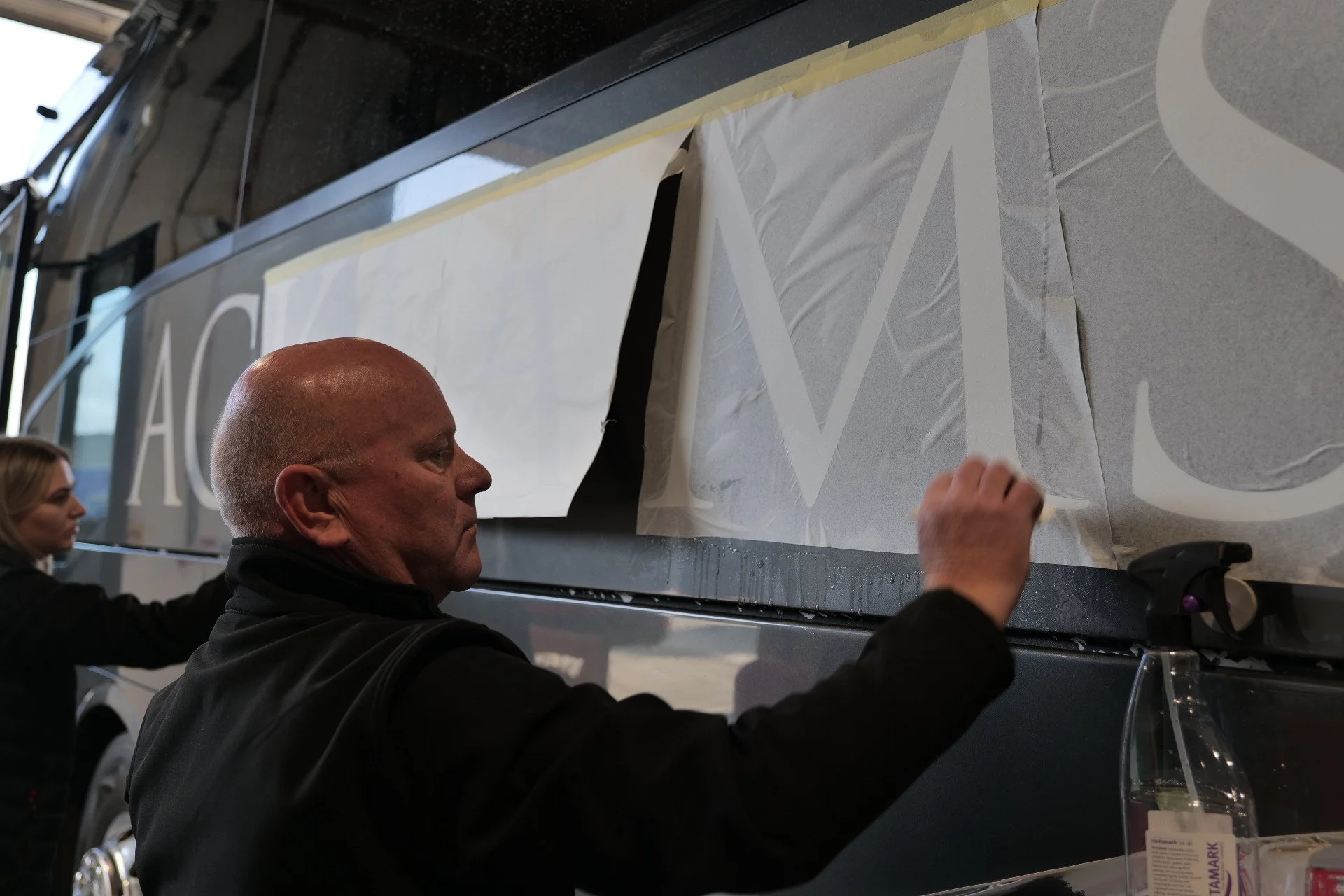 Two people applying vinyl lettering to the side of a vehicle.