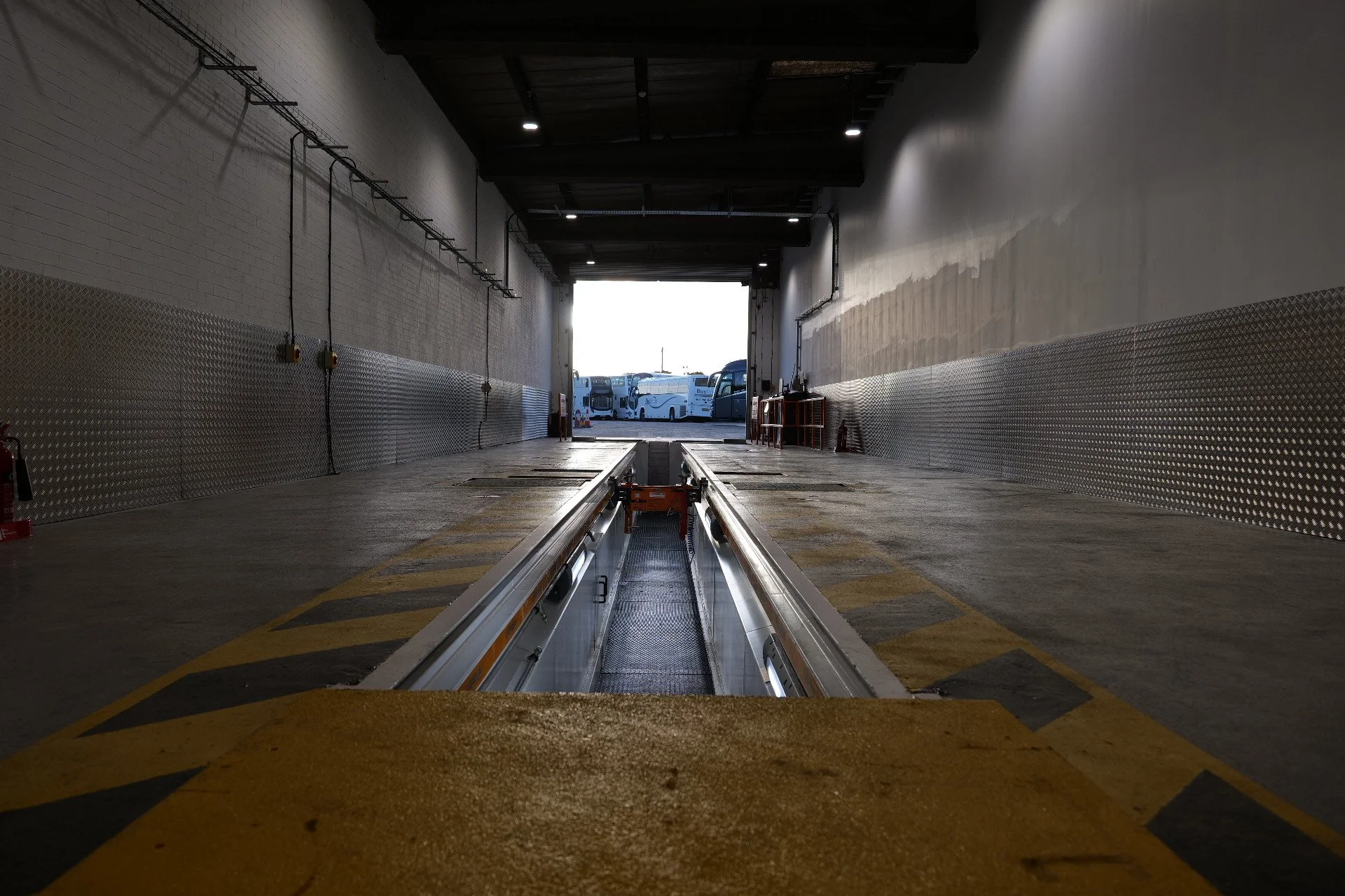 View inside a loading dock of a storage facility, looking toward an open garage door where buses are parked outside in daylight.