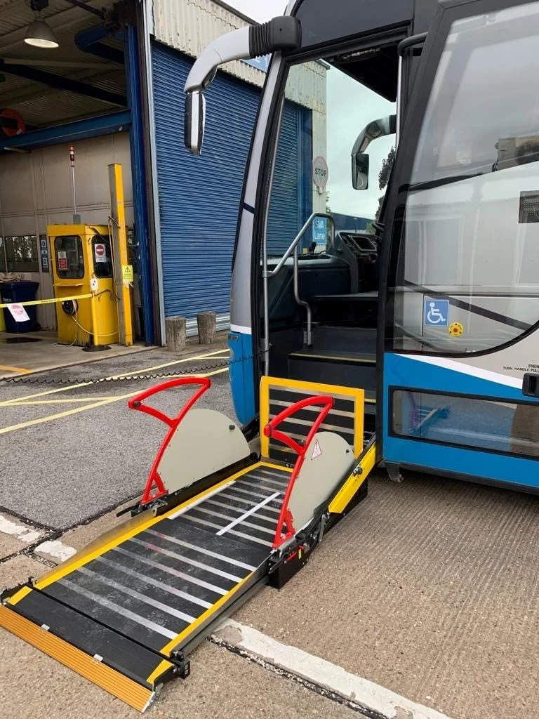 Public transit bus with a wheelchair lift deployed in front of a loading area with a blue industrial garage door.
