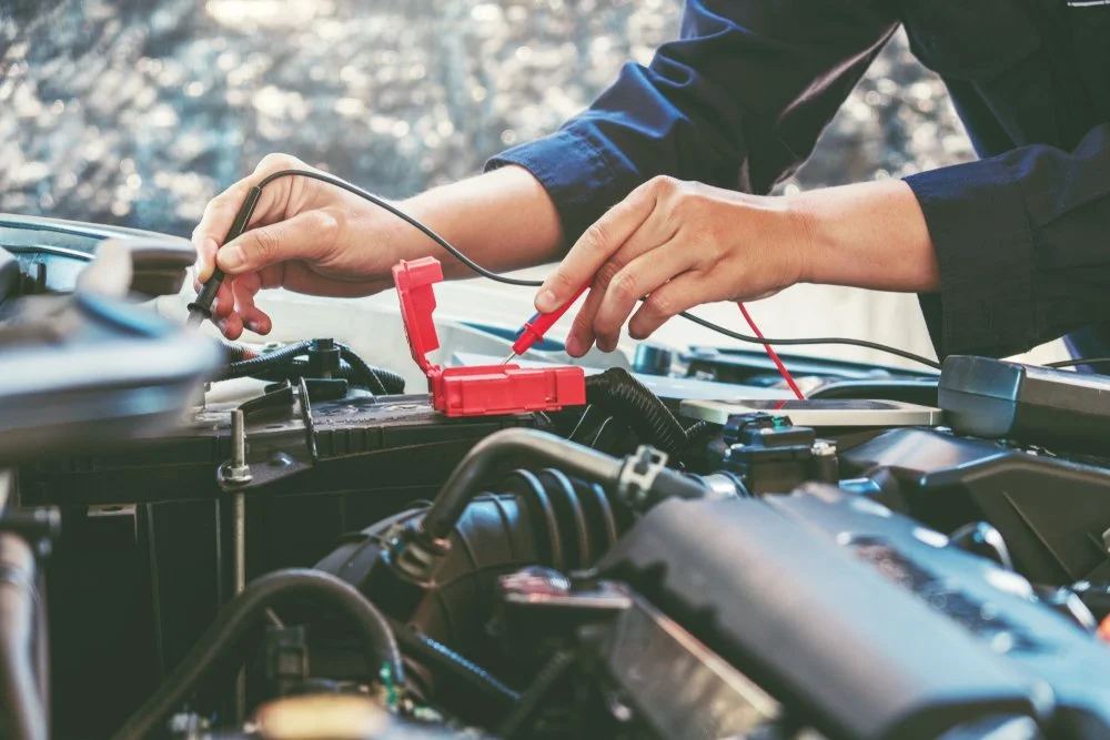 Person checking car battery with multimeter cables in an outdoor setting.