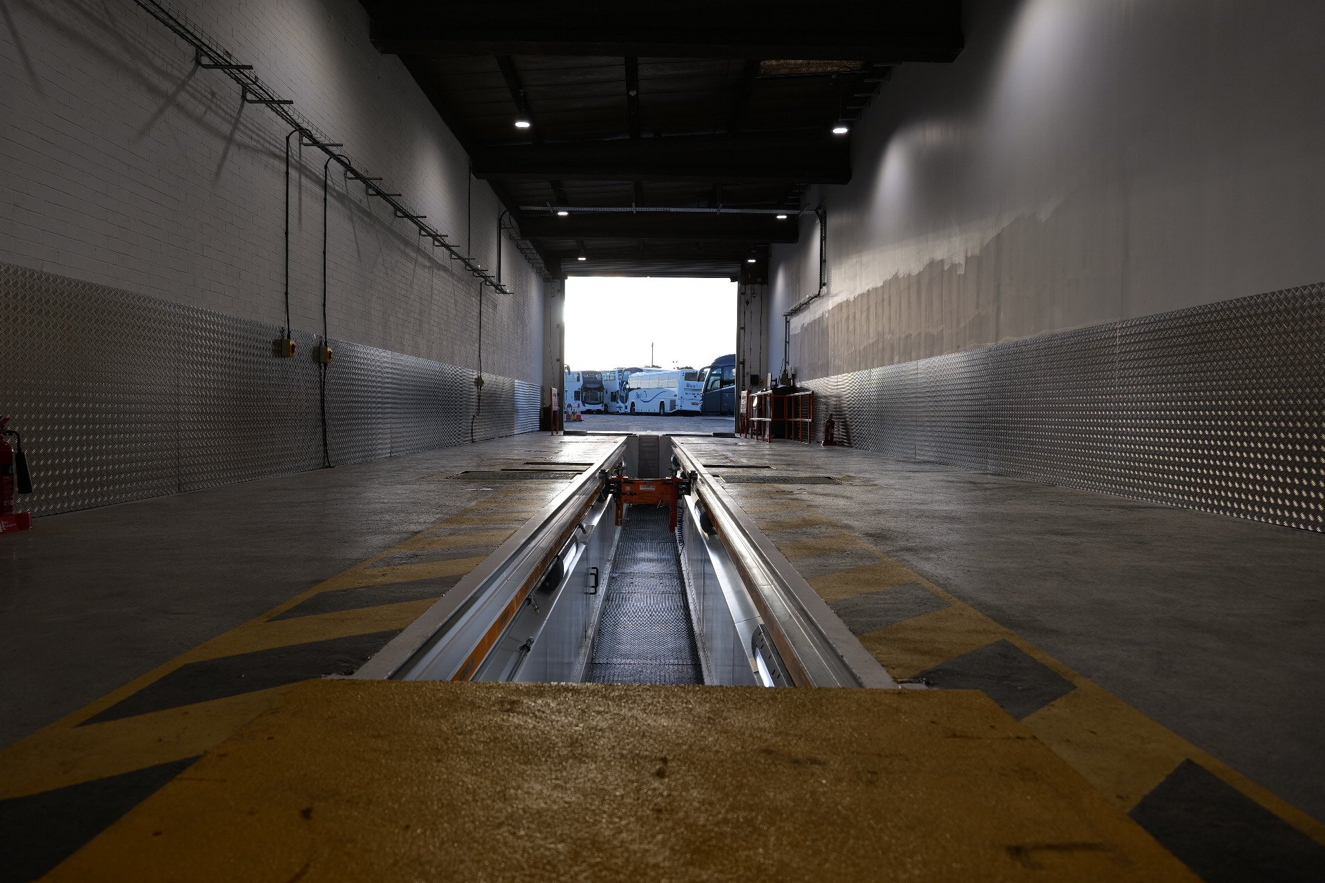 View inside a loading dock with an open bay door showing parked buses outside.